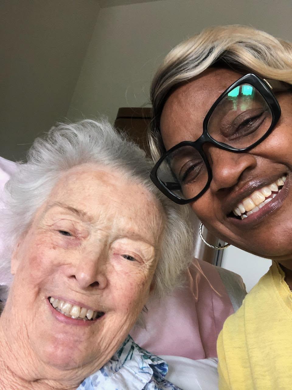 Two women share a warm smile in a care facility room, enjoying their time together.