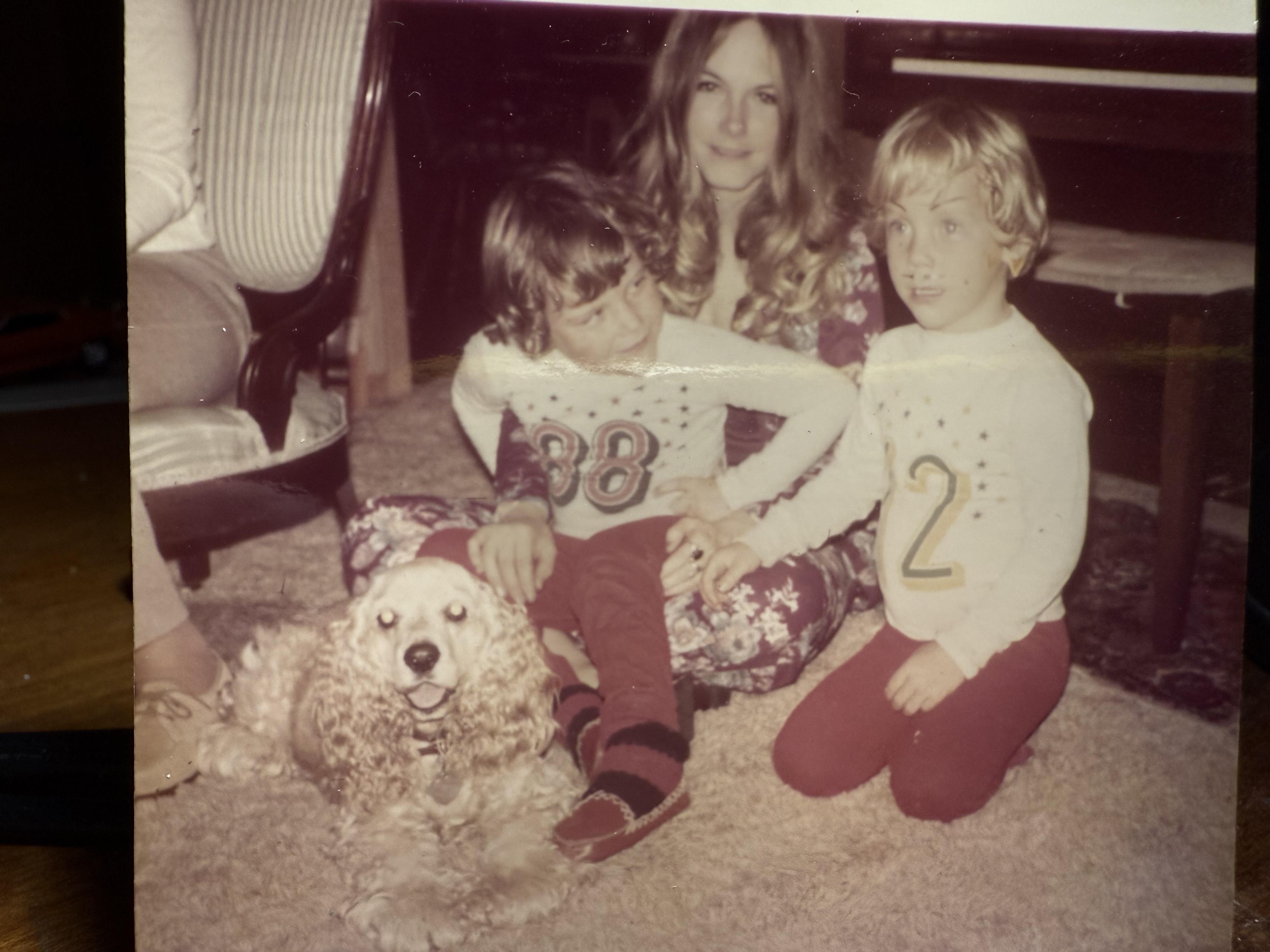 Children in matching outfits sit on a carpet with a dog and an adult in a warm living room.