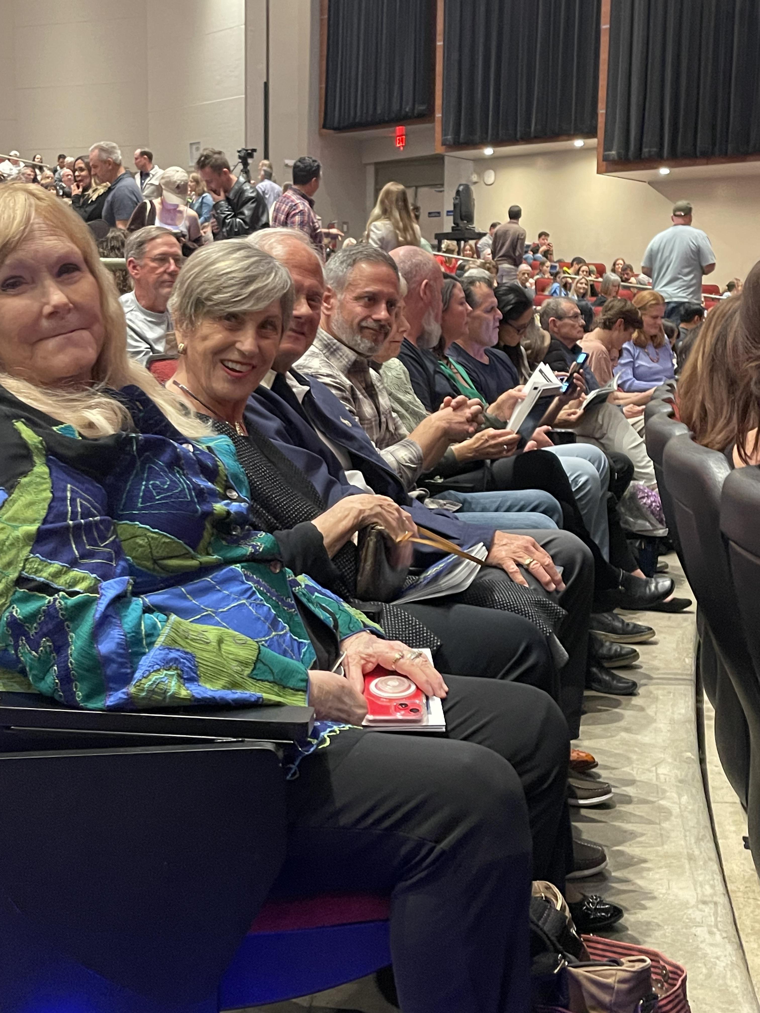 Attendees chat and smile in a packed auditorium, eagerly awaiting the presentation.