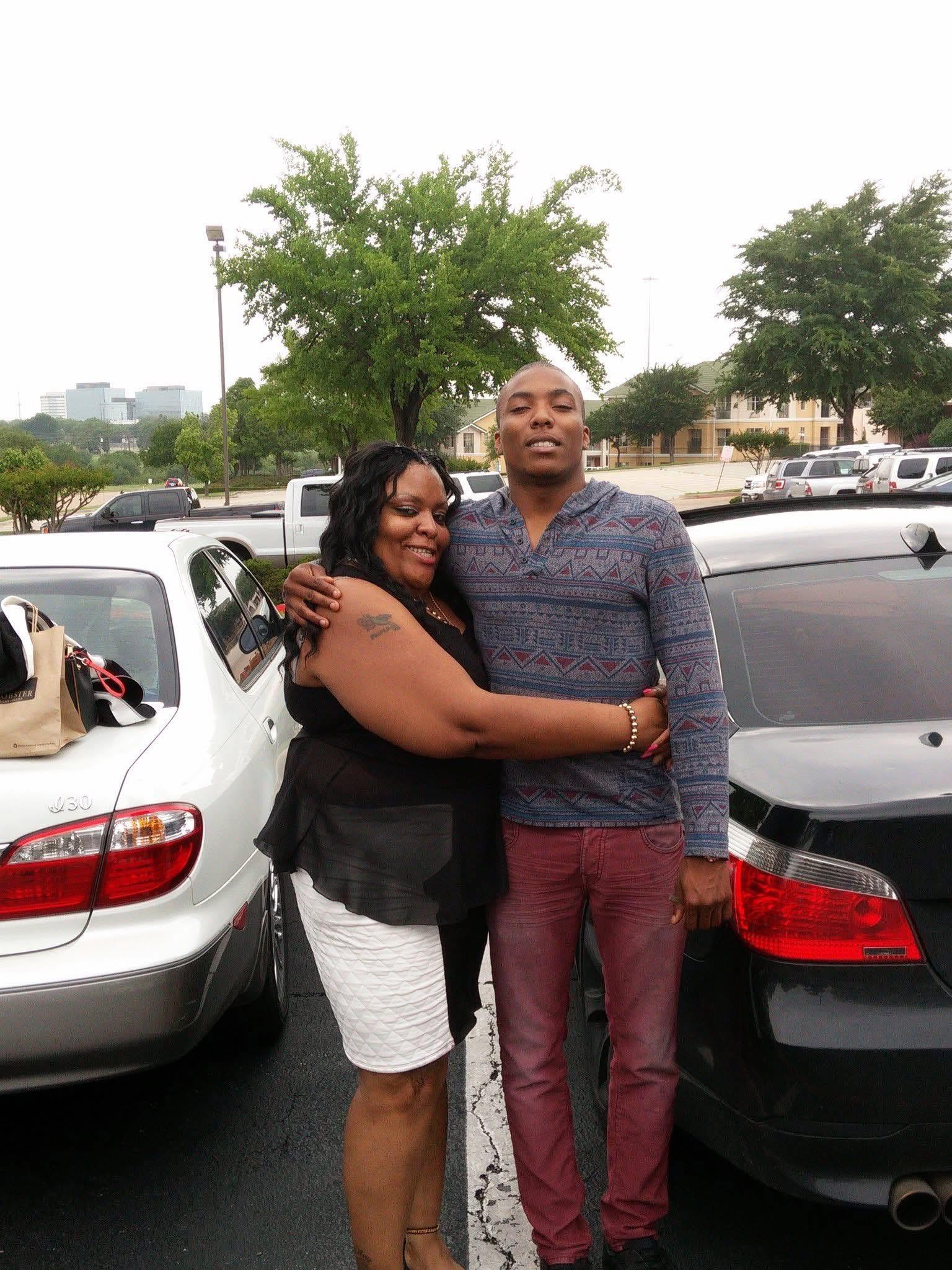 Couple stands close together, smiling joyfully in a busy parking lot during overcast weather.