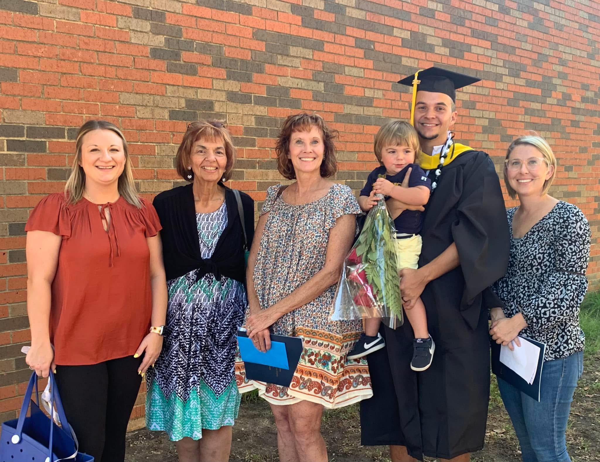 Family members gather to celebrate a graduation milestone with smiles and flowers under sunlight.
