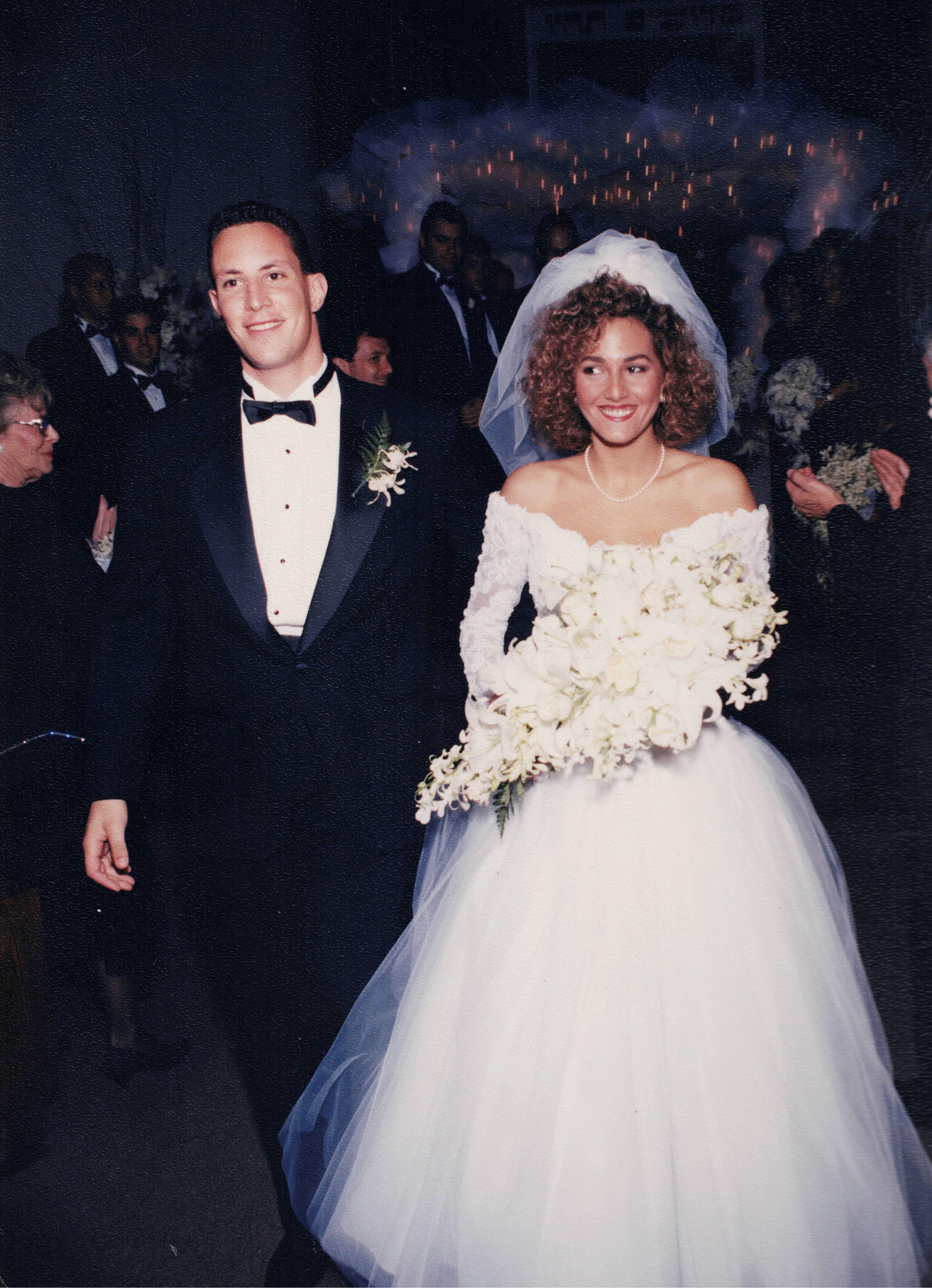 An elegantly dressed couple strolls down the aisle, joyful and surrounded by celebrating guests.