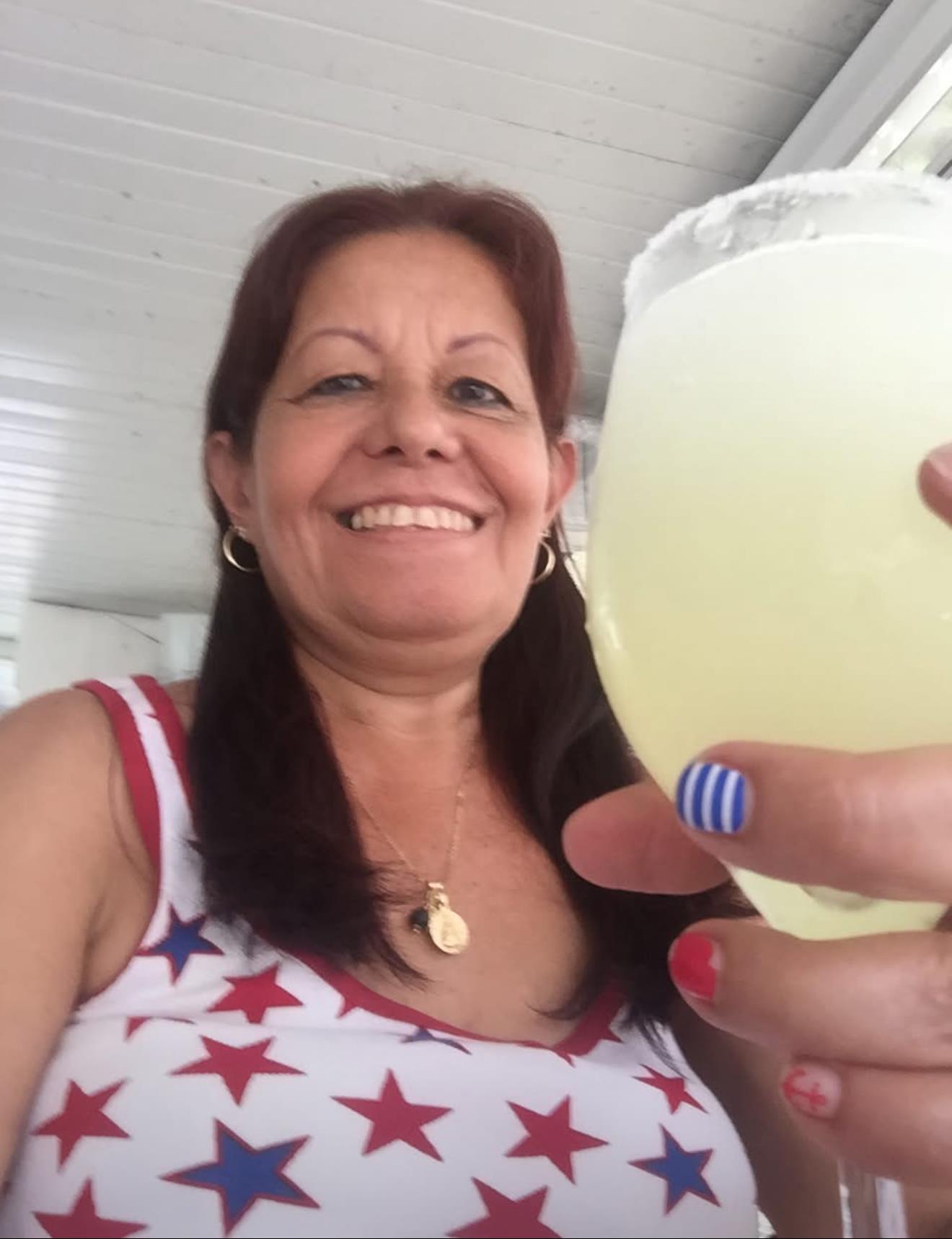A woman dressed in a star-patterned outfit raises a glass with a cocktail, smiling joyfully.