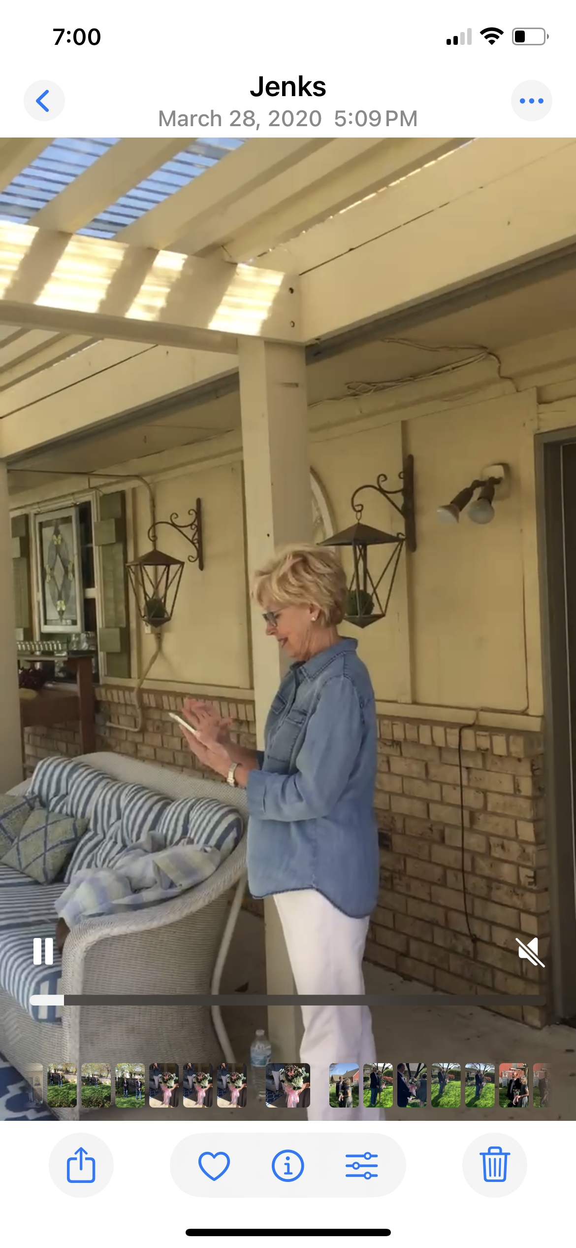 A woman in casual attire is absorbed in her phone while outside in a cozy garden area.