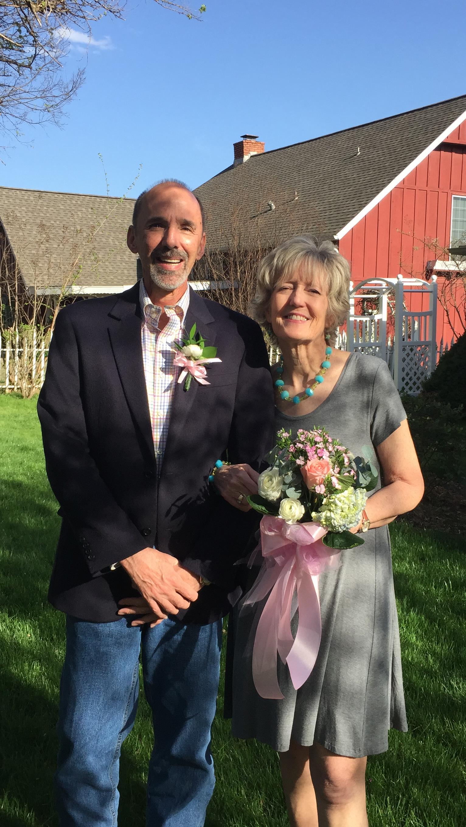 A joyful couple poses together in a garden, wearing formal attire and smiling happily.