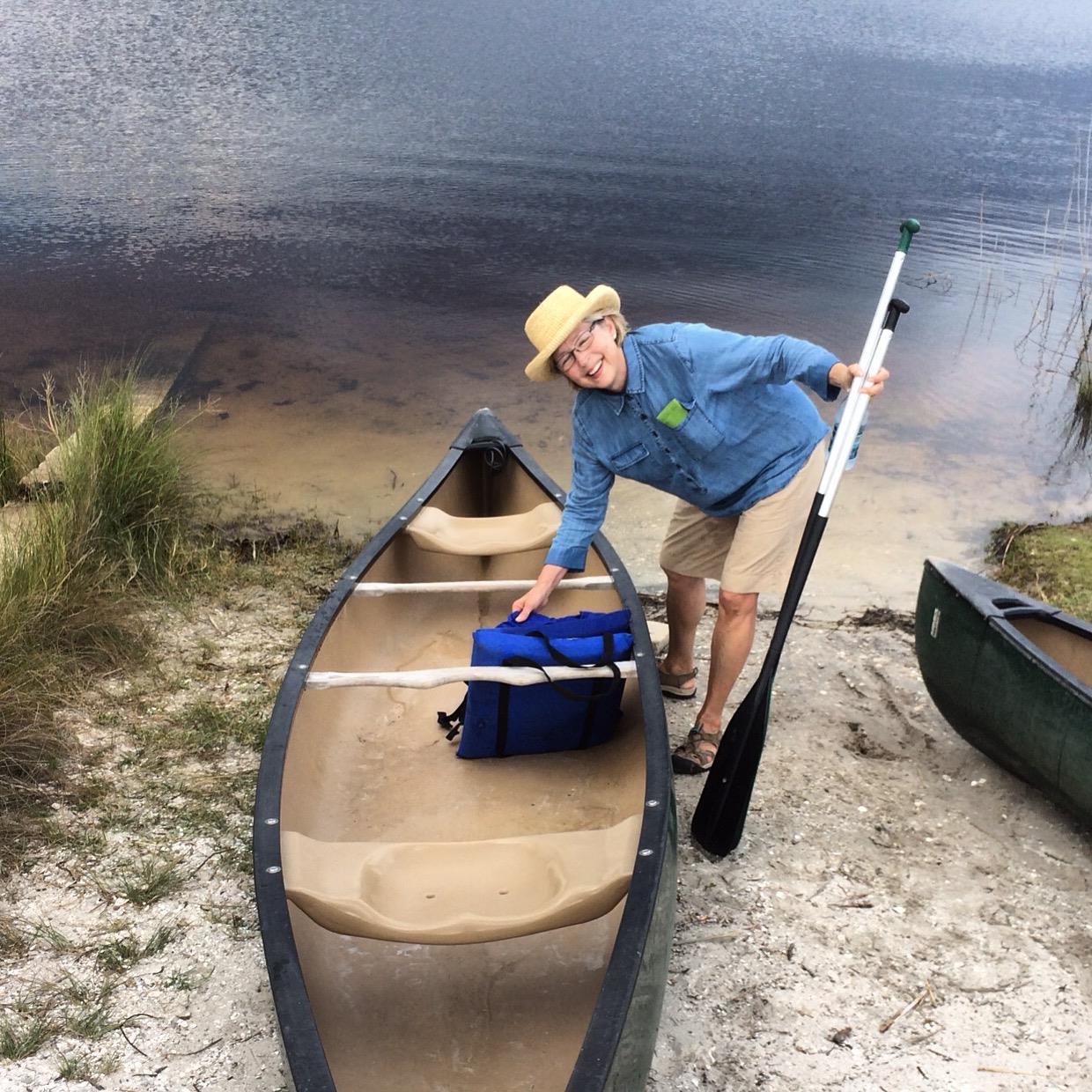 An older man stands beside a canoe, readying his gear for an afternoon of paddling on the lake.