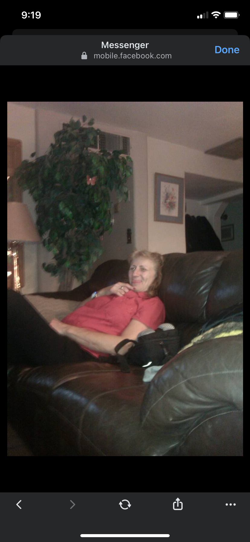 A woman relaxes on a brown couch in a living room. She enjoys her time with a smile.