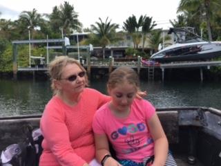 Two women sit comfortably on a boat, surrounded by lush greenery and luxury boats.