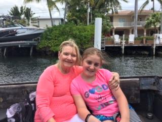 Two women sit together on a boat, smiling on a sunny day by the palm-lined water.