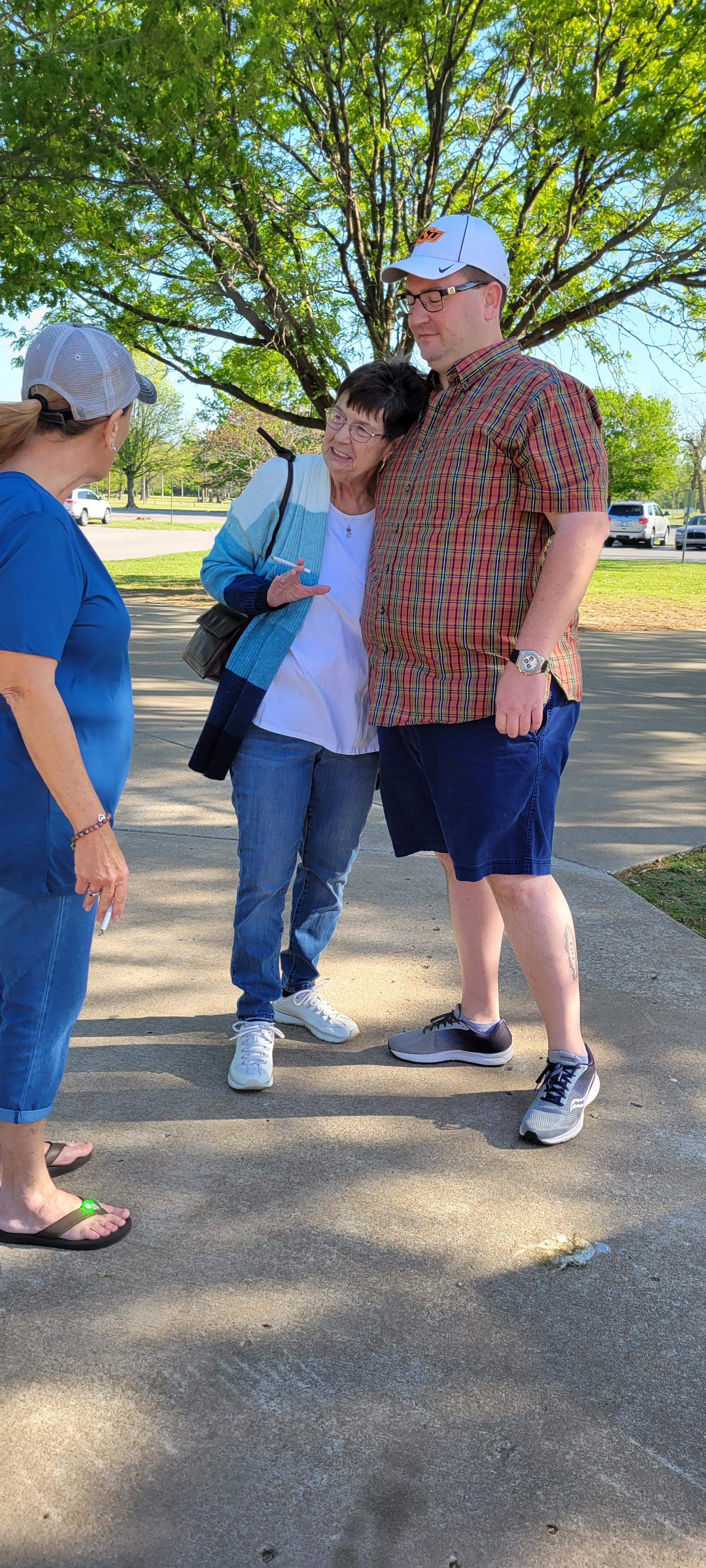 Three friends share a warm moment in the park with smiles and laughter on a sunny day.