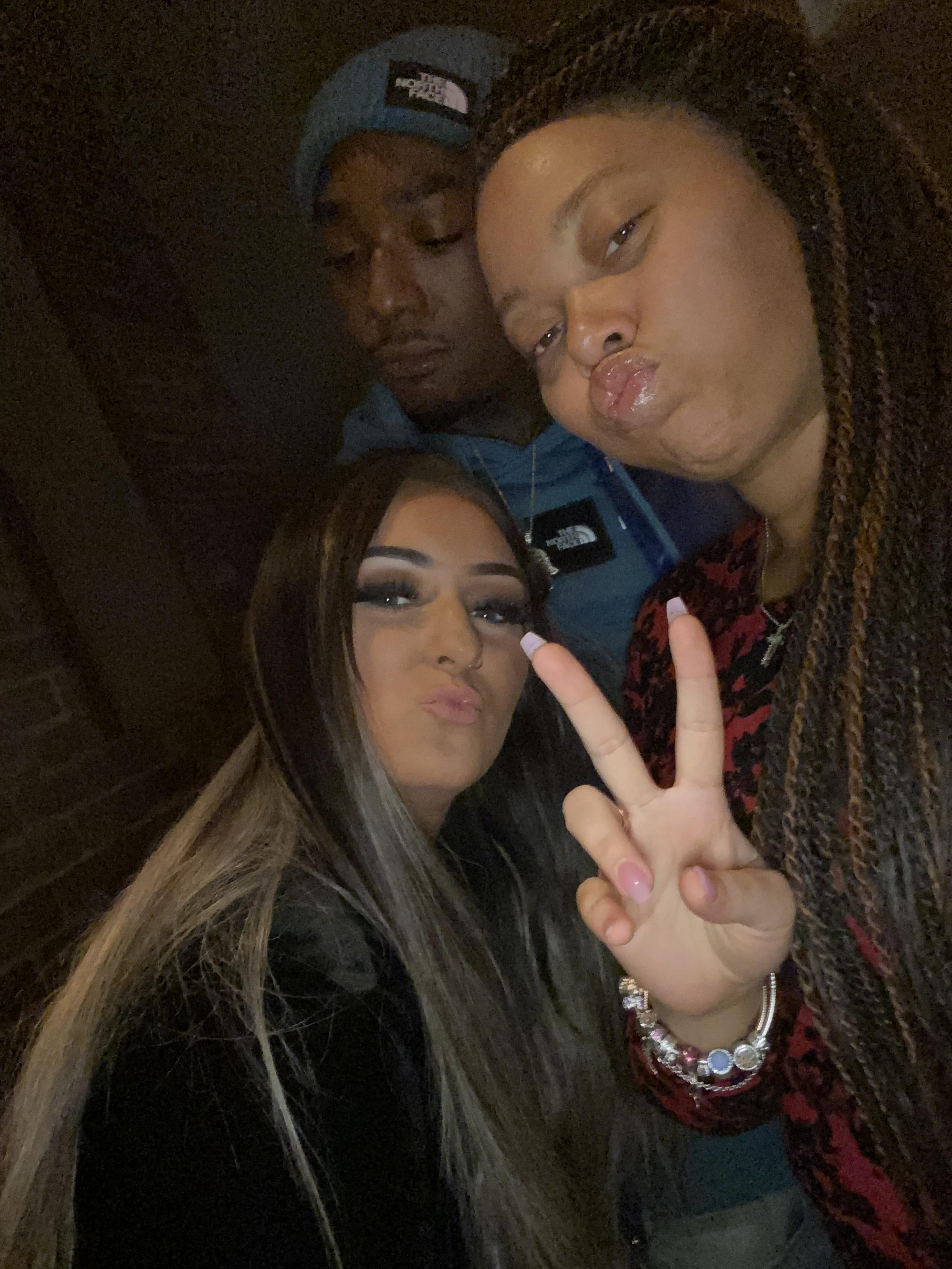 Three friends strike fun poses together in a casual outdoor setting at night.