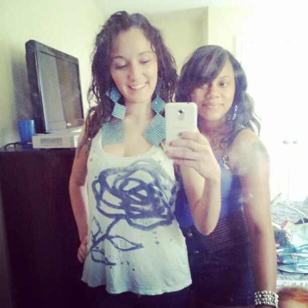 Two women stand together, each displaying unique styles, and share smiles while taking a selfie.