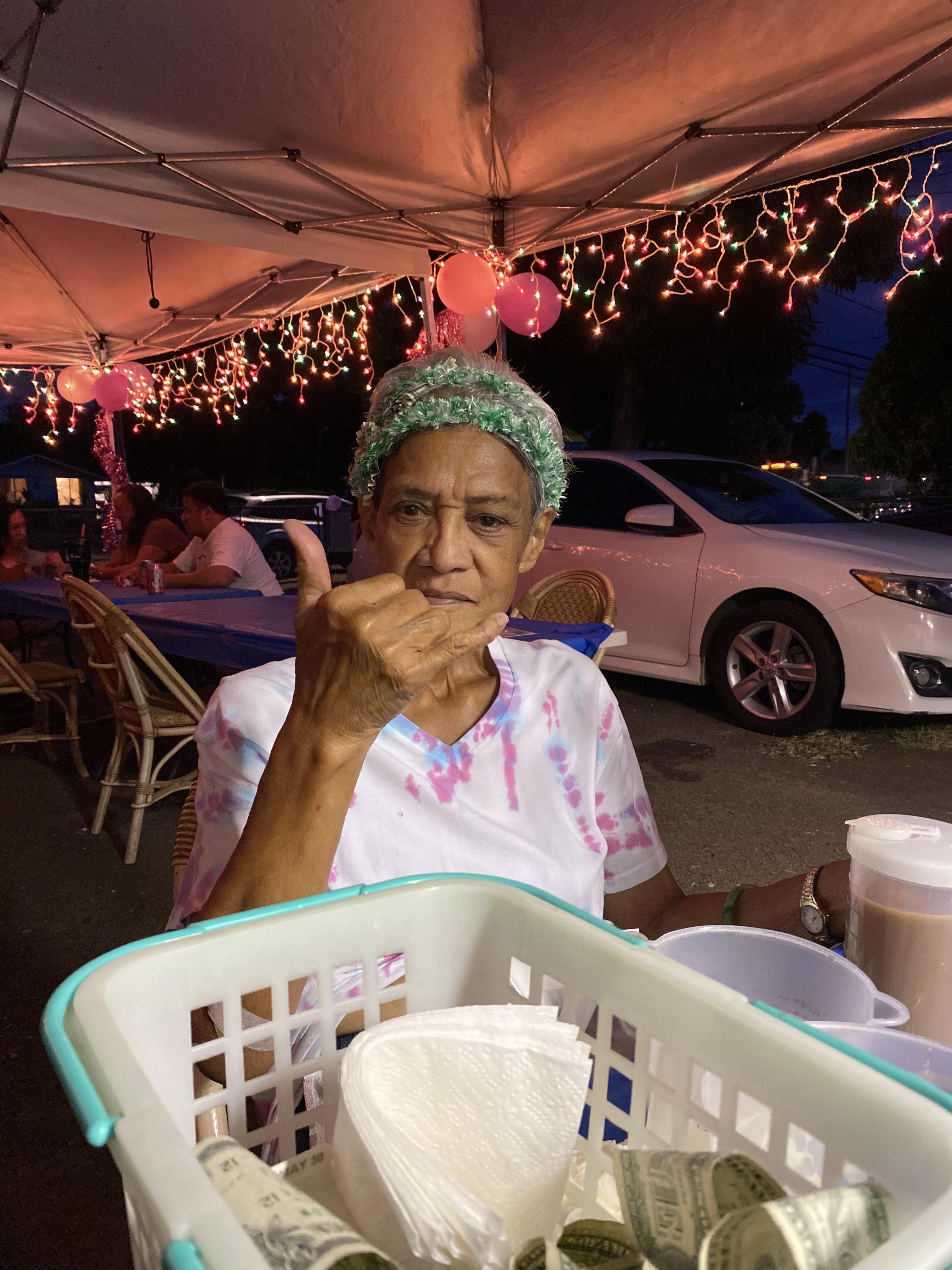 Woman sits at a table with drinks and gestures happily during a local event at night.