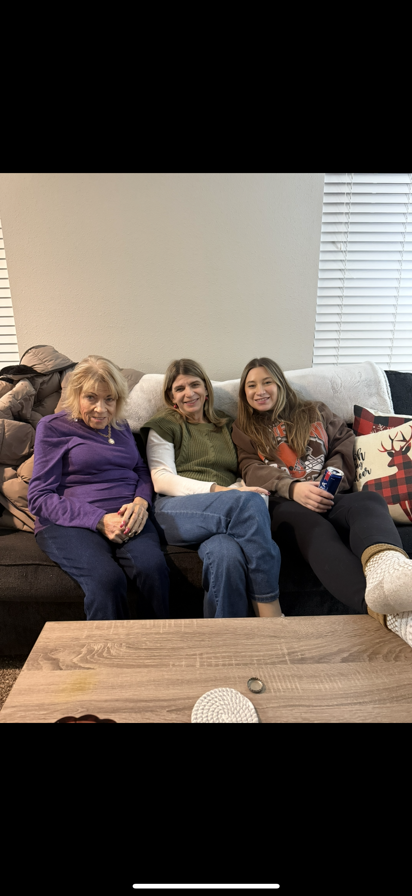 Three family members sit comfortably on a couch, sharing smiles and laughter at home.