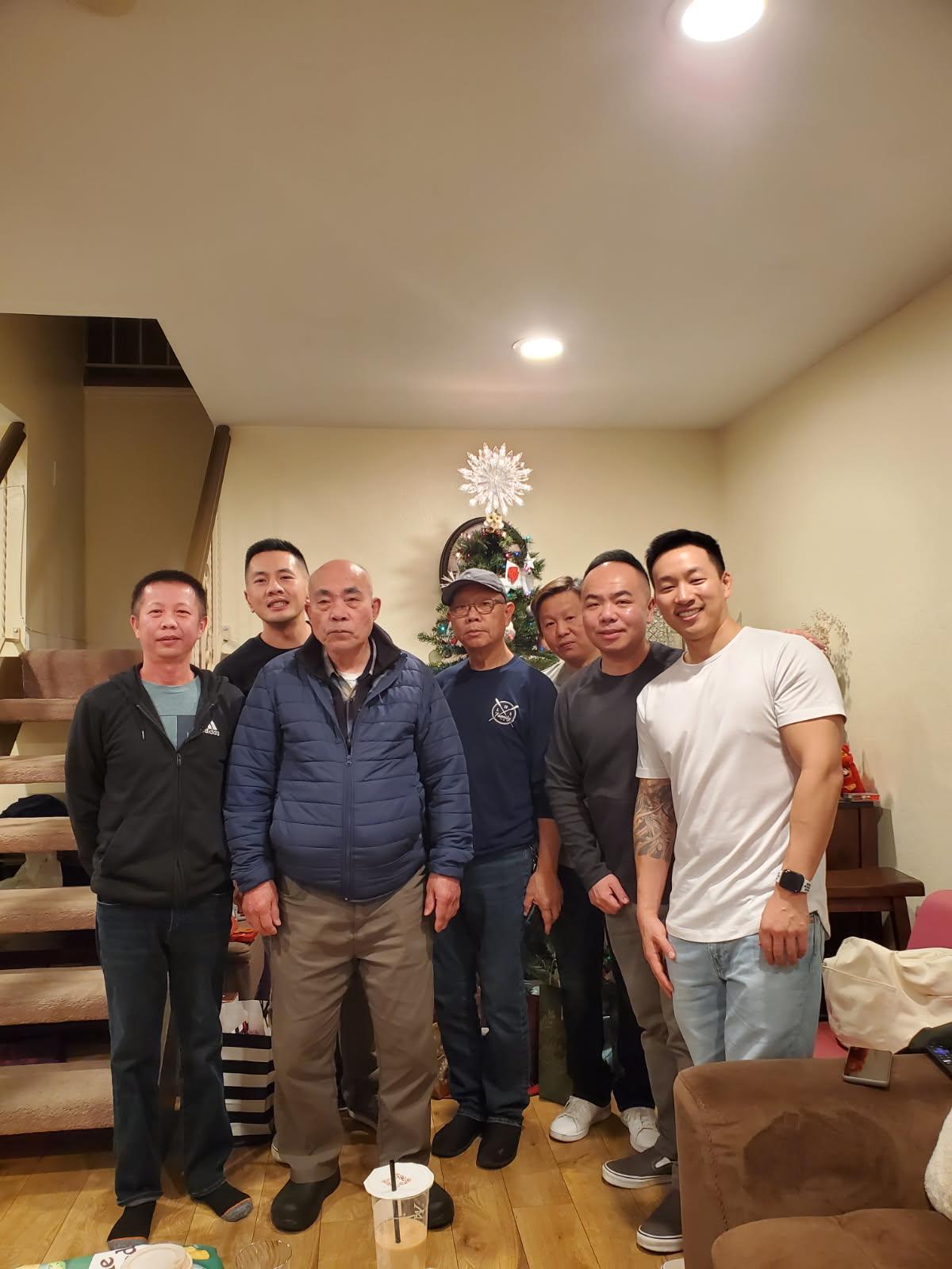 Group of seven men posing together in a decorated living room, celebrating the holiday season.