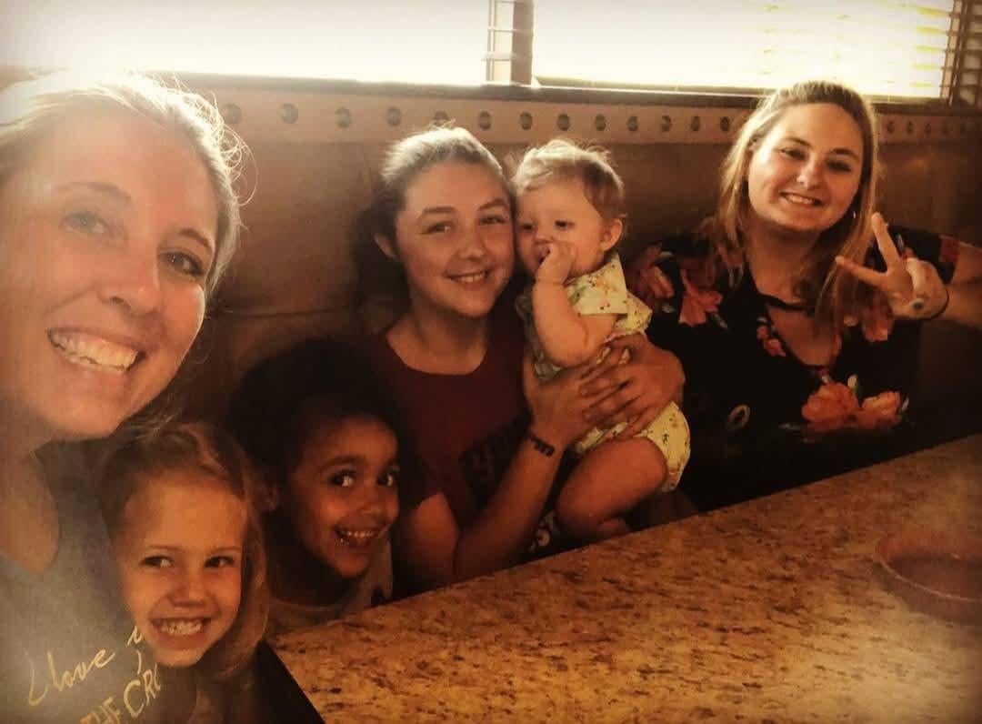 A group of cheerful women and children gather around a table, sharing smiles and laughter.
