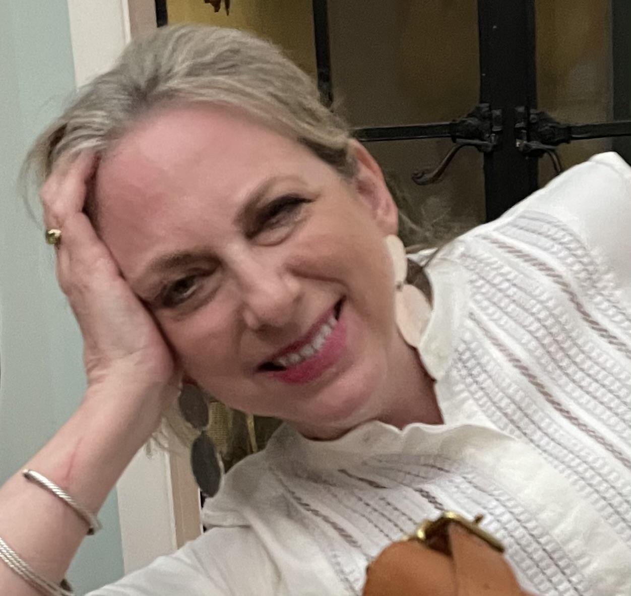 A woman enjoys a light moment indoors, wearing a white blouse and smiling warmly at friends.