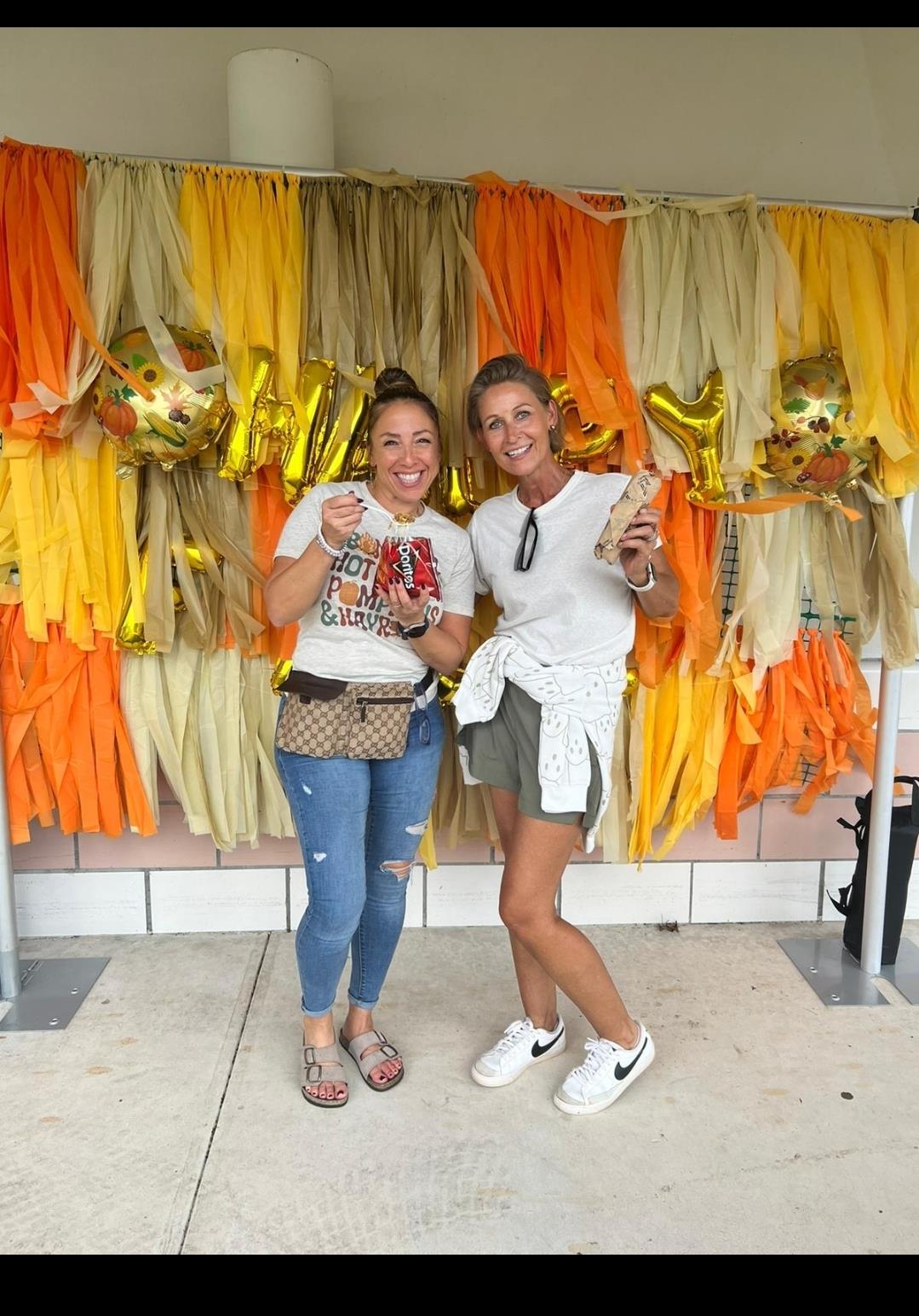 Two friends pose with treats against a bright backdrop during a joyful outdoor celebration.