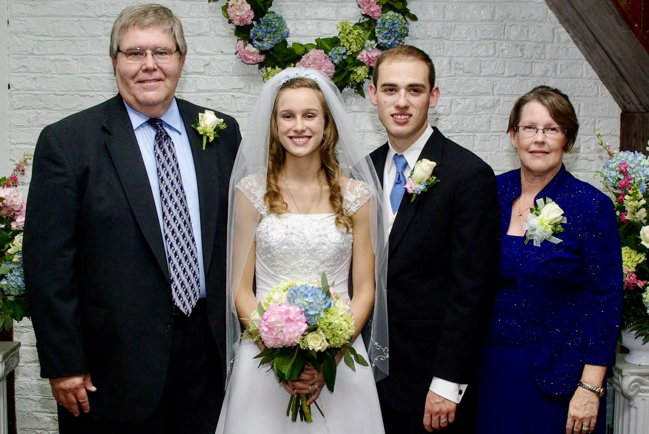 A bride and groom pose happily with family members in a decorated indoor setting.