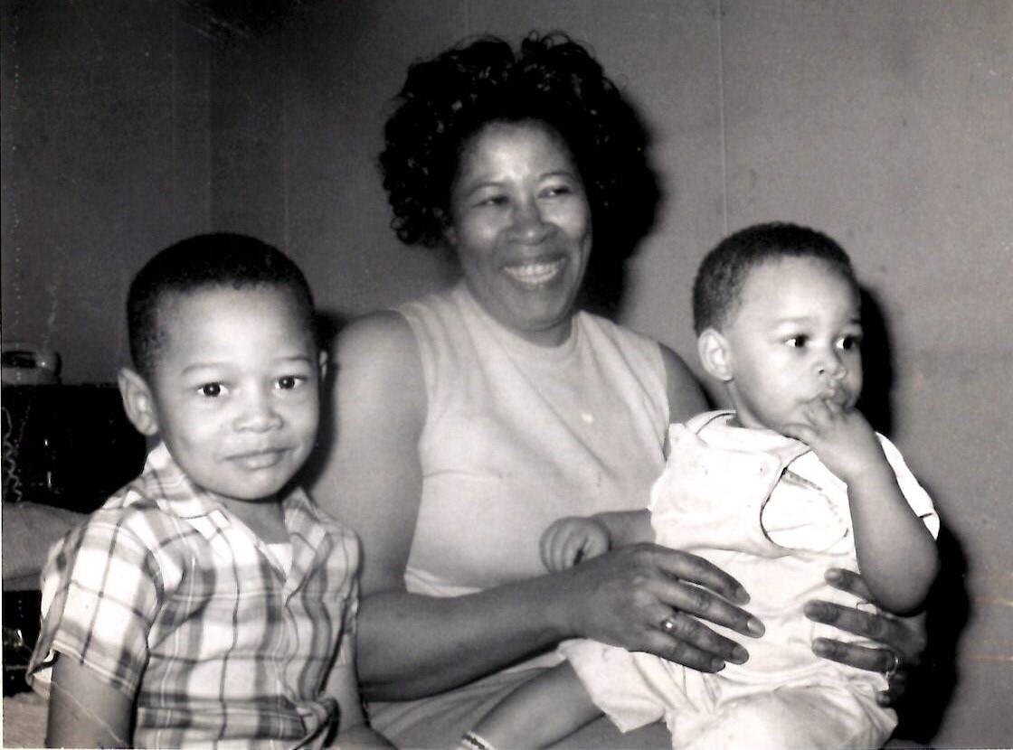 A woman smiles warmly while holding two young boys, creating a heartwarming family atmosphere.