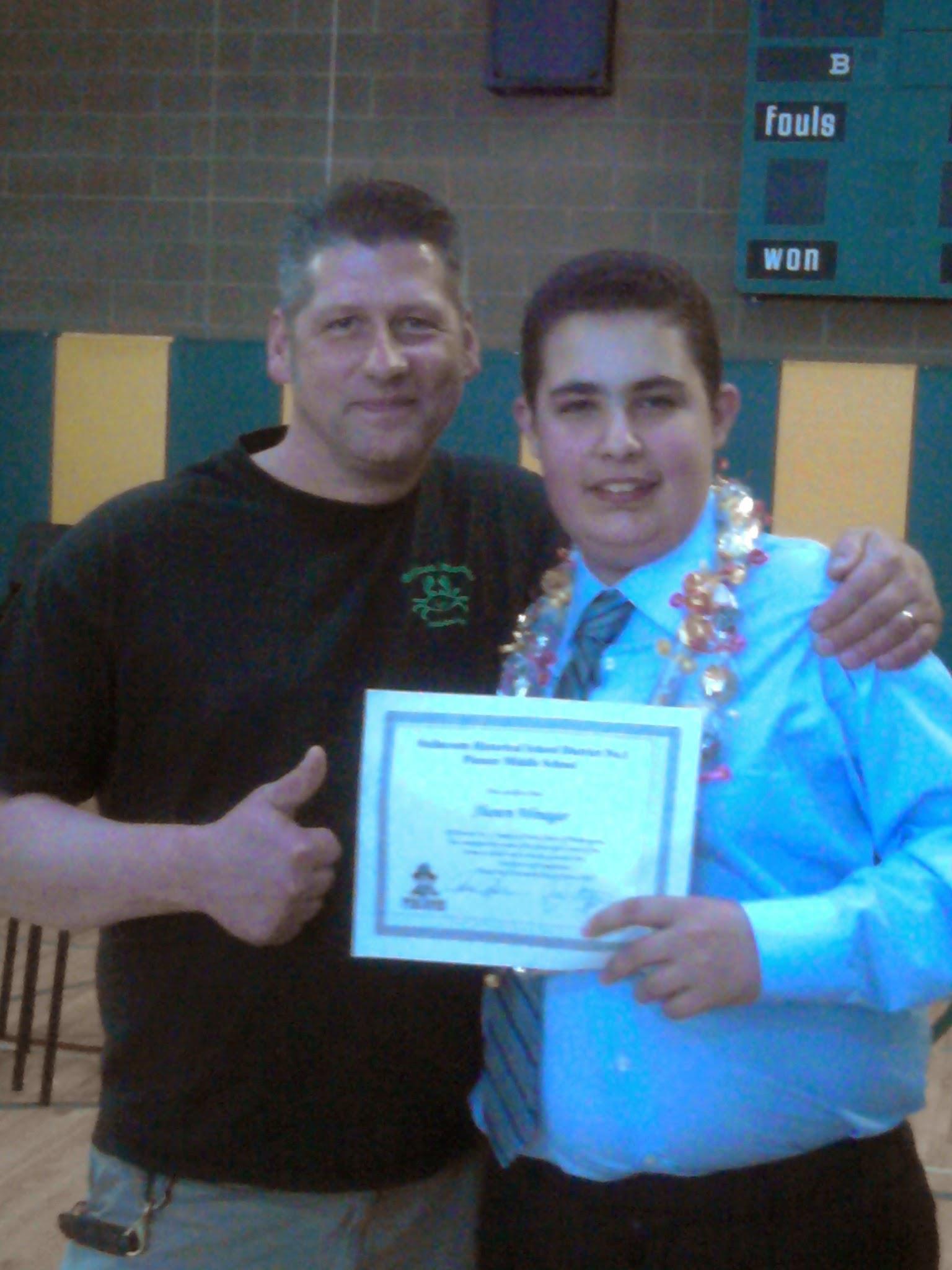 A young student receives a certificate while posing with a proud adult family member.