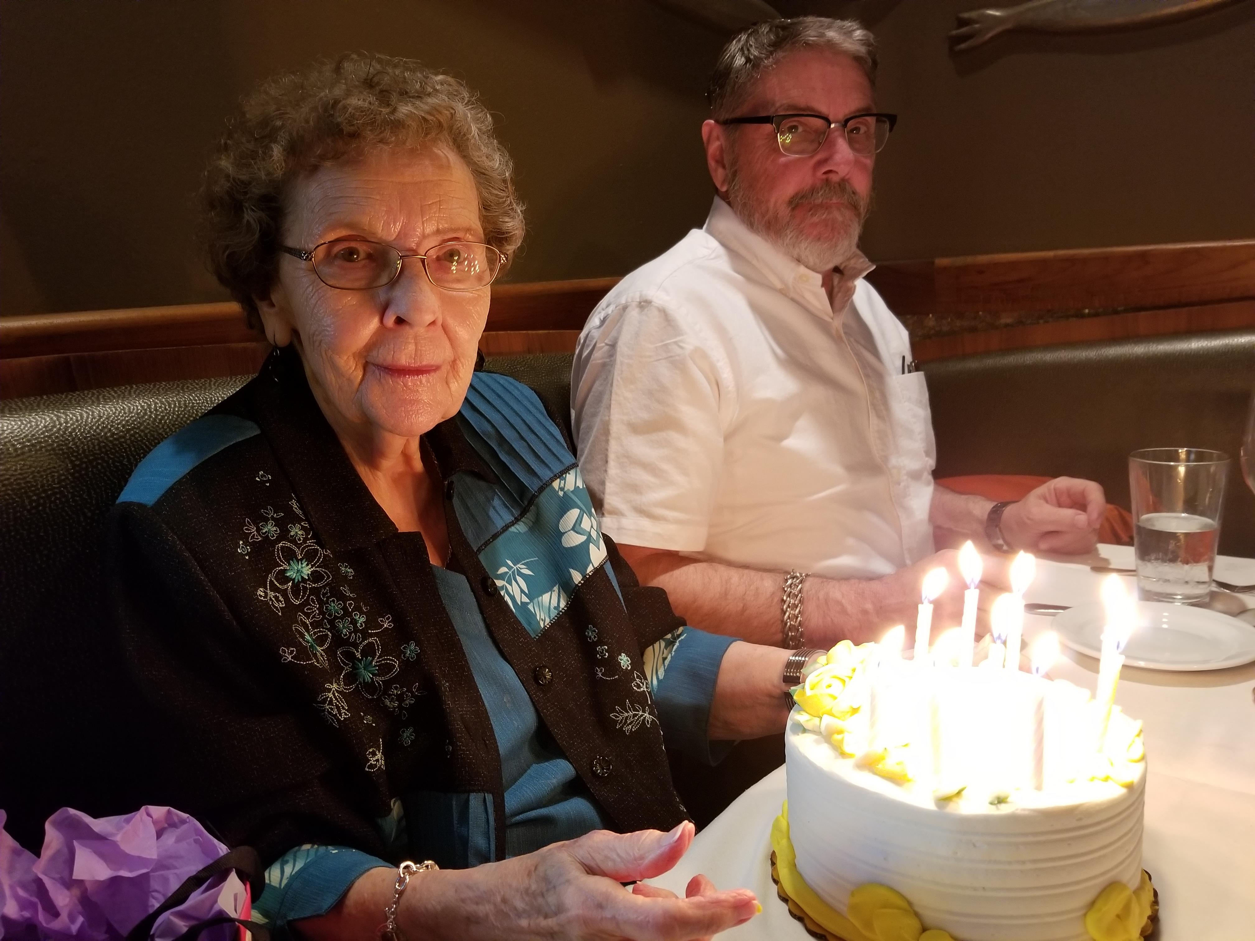 A woman celebrates her birthday with family at a restaurant, surrounded by a beautiful cake.