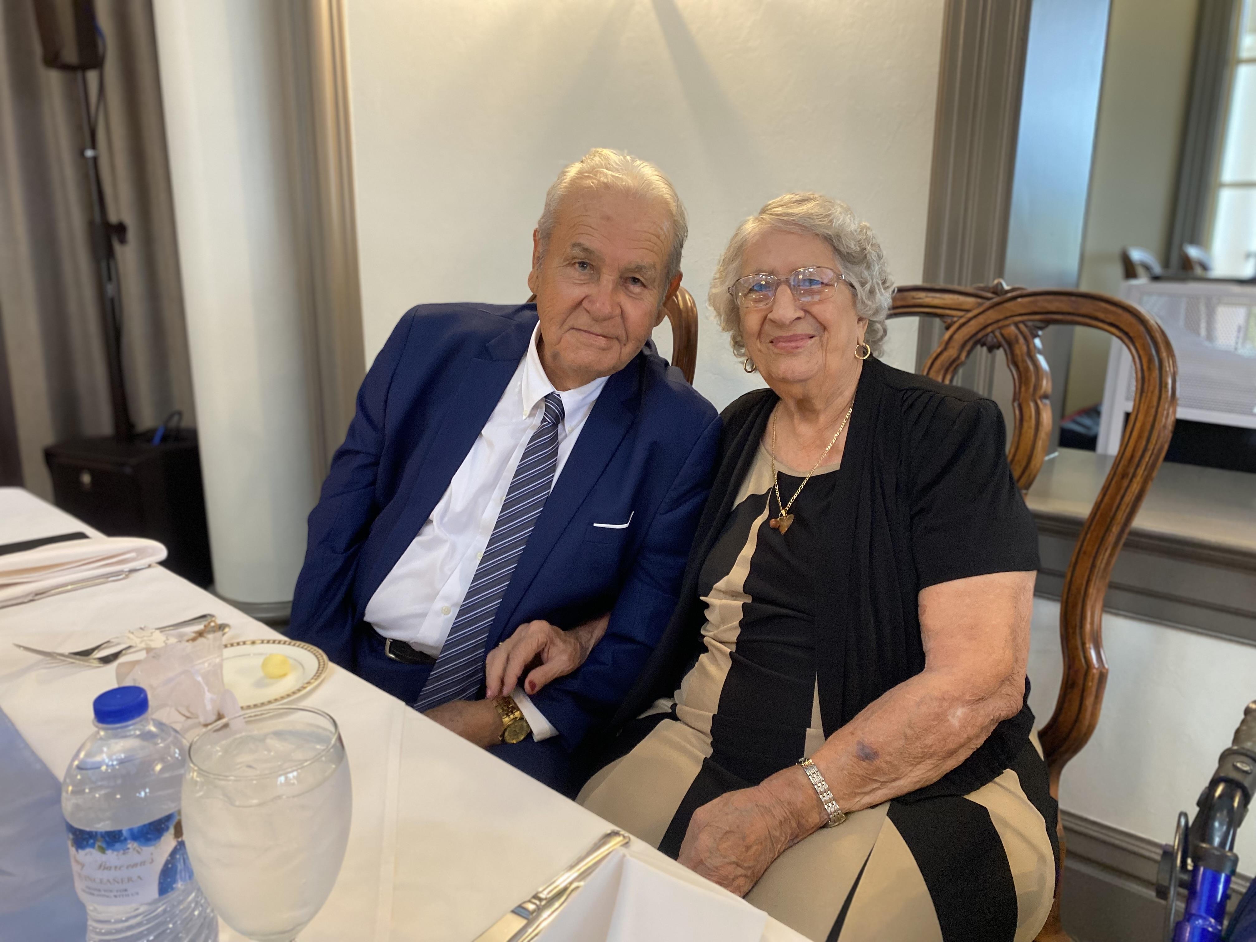 Joyful elderly couple poses closely together at a nicely set dining table in a sophisticated venue.