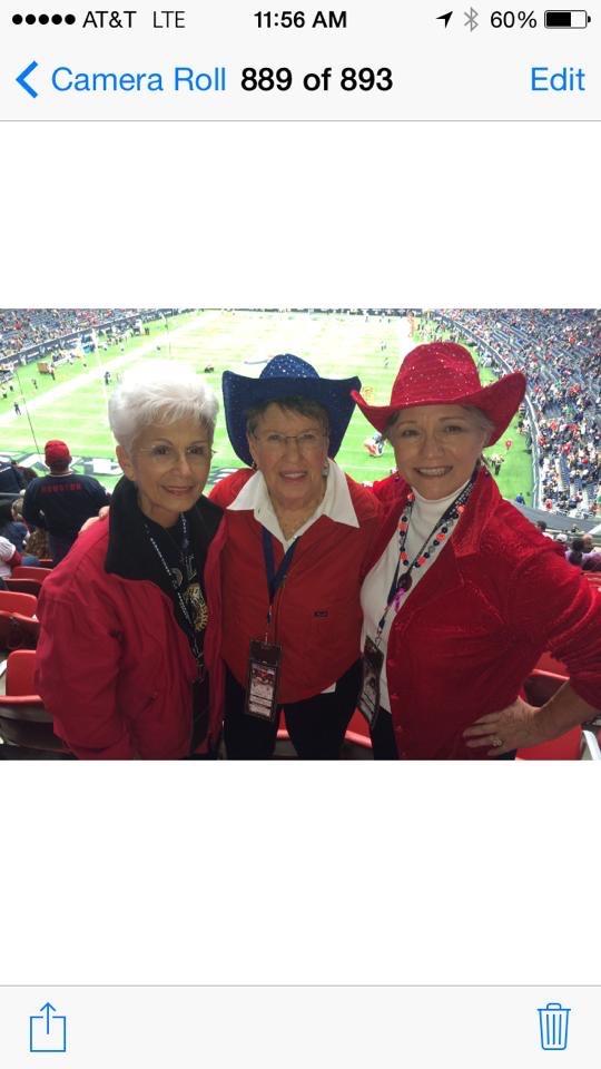 Three friends pose happily at a football game, wearing colorful hats and team colors.