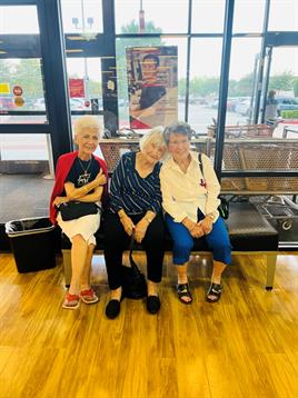 Three friends share laughter while sitting together on a bench in a store during the afternoon.