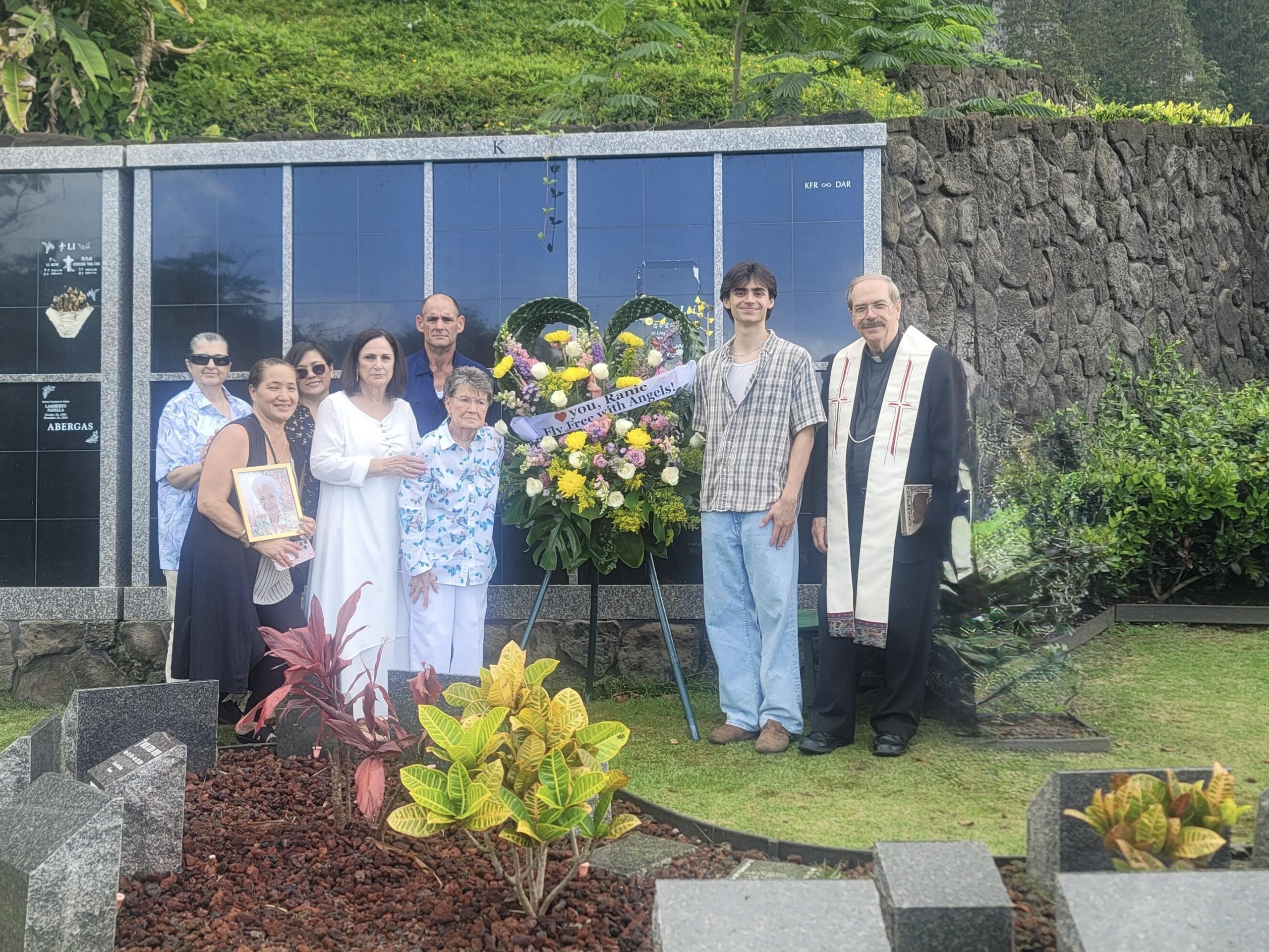 A family gathers at a memorial, surrounded by flowers, honoring their loved one.