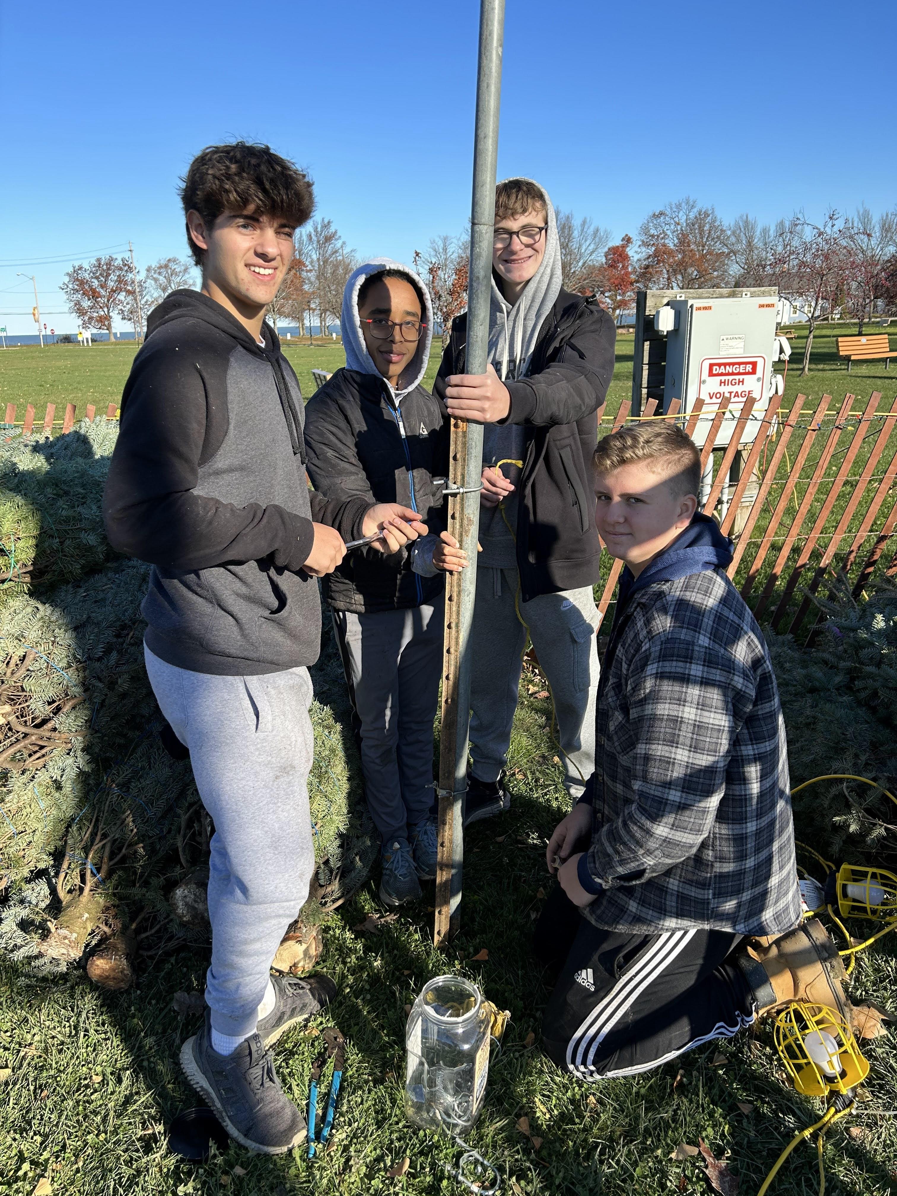 Four students work together to plant a tree in a park during a clear, sunny fall day.
