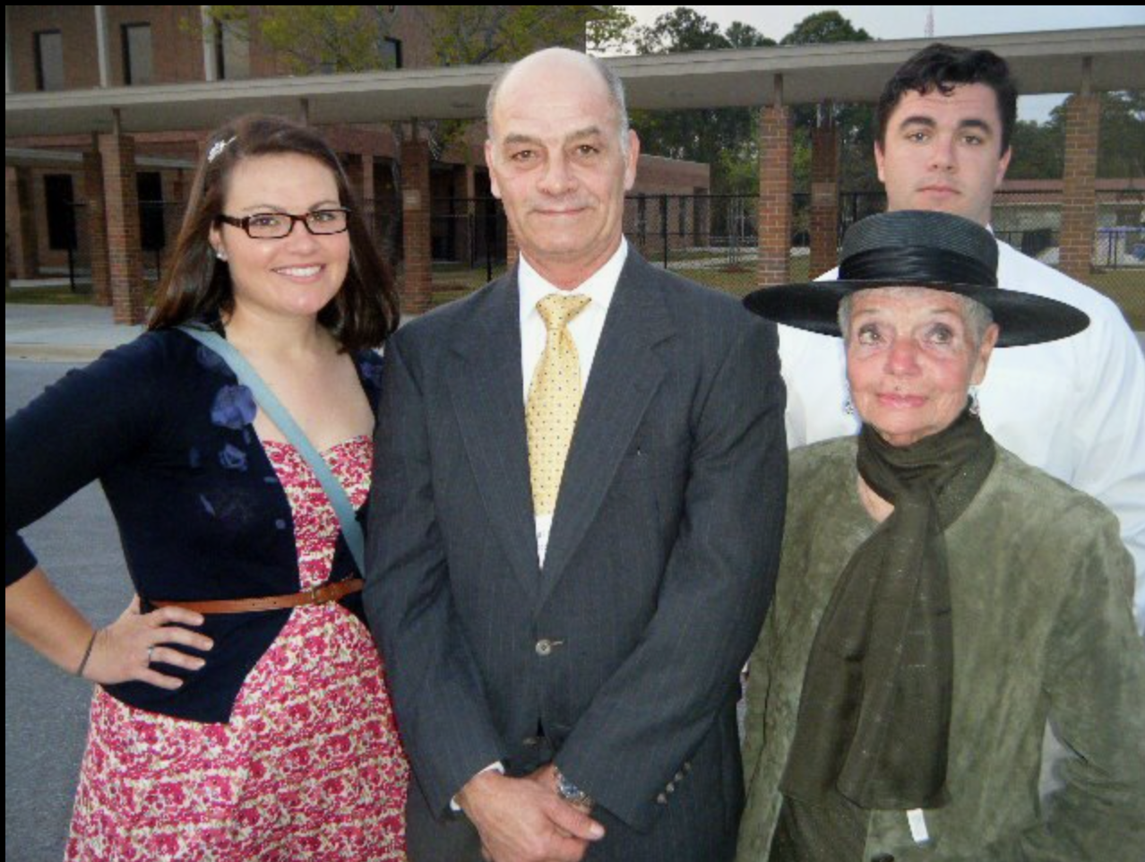 Four family members dressed in formal attire stand together, smiling in a park setting at dusk.