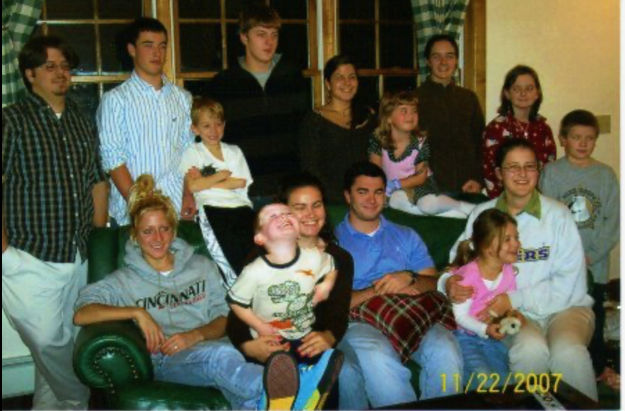 A large group of family members poses together on a green couch, smiling and enjoying their time.