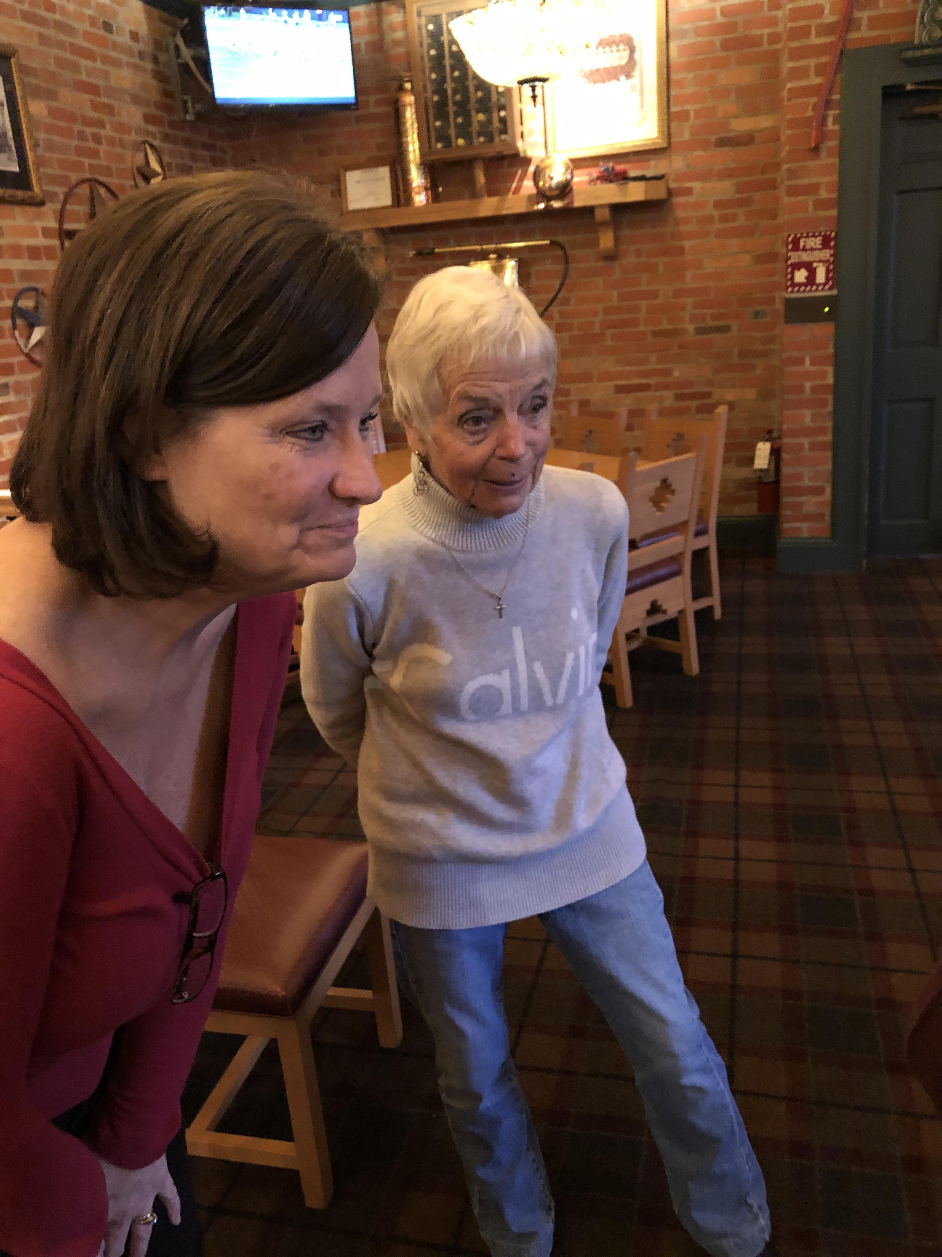 Two women, one older and one younger, watch intently in a warm restaurant.