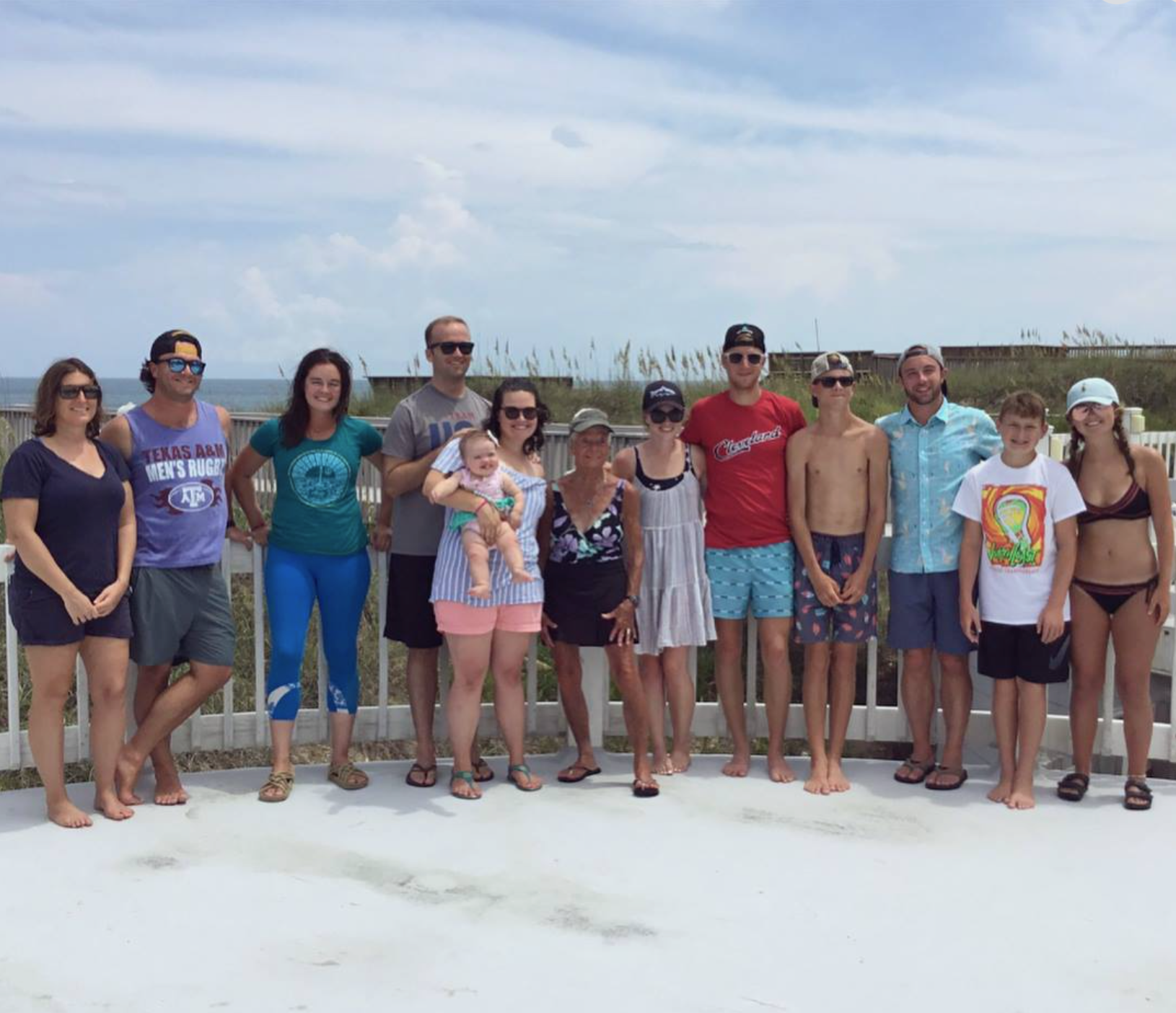Family members smiling on a beach deck with the ocean and blue sky in the background.