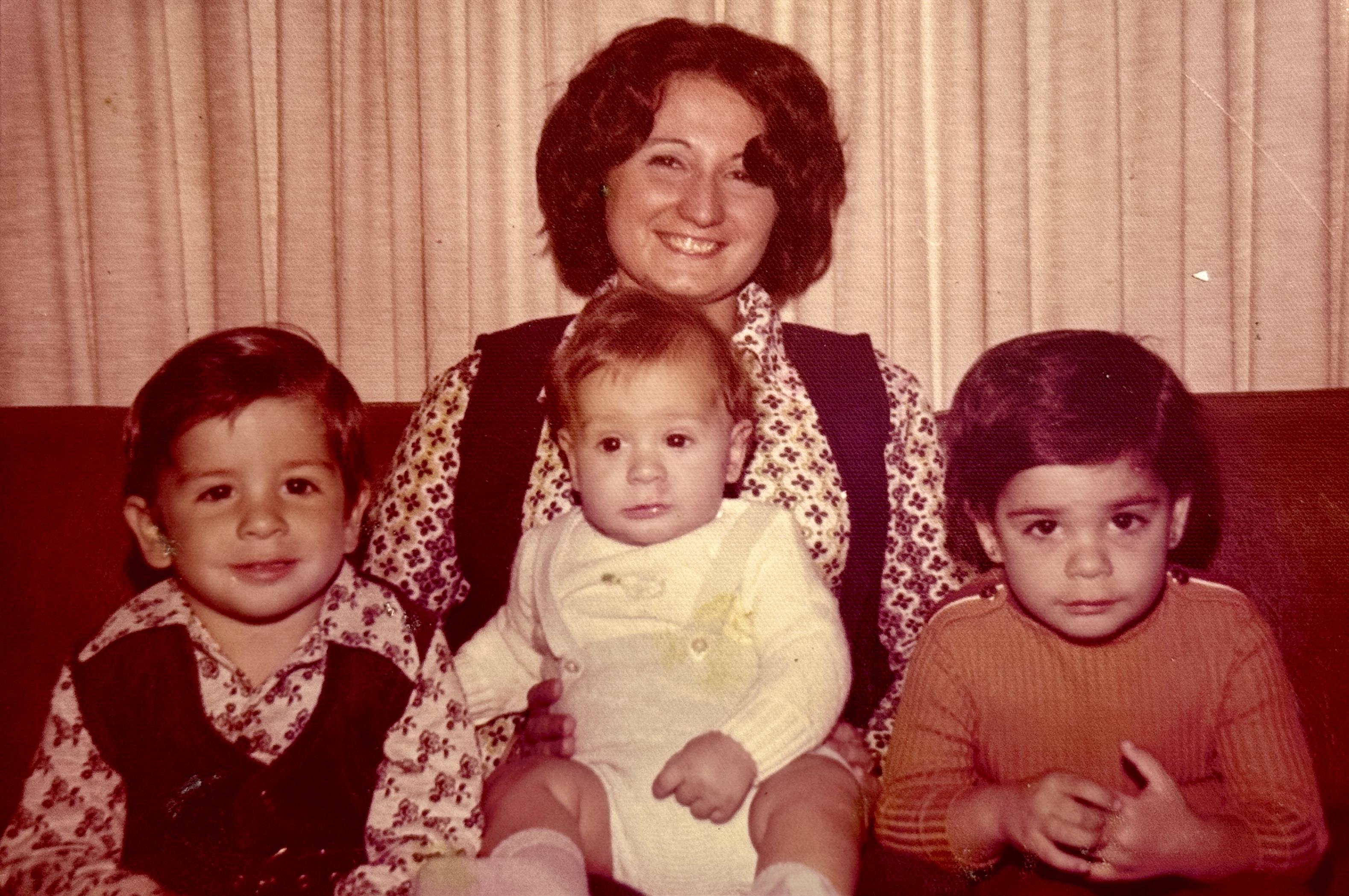A smiling mother sits with her three children, showcasing a nostalgic family moment in the 1970s.