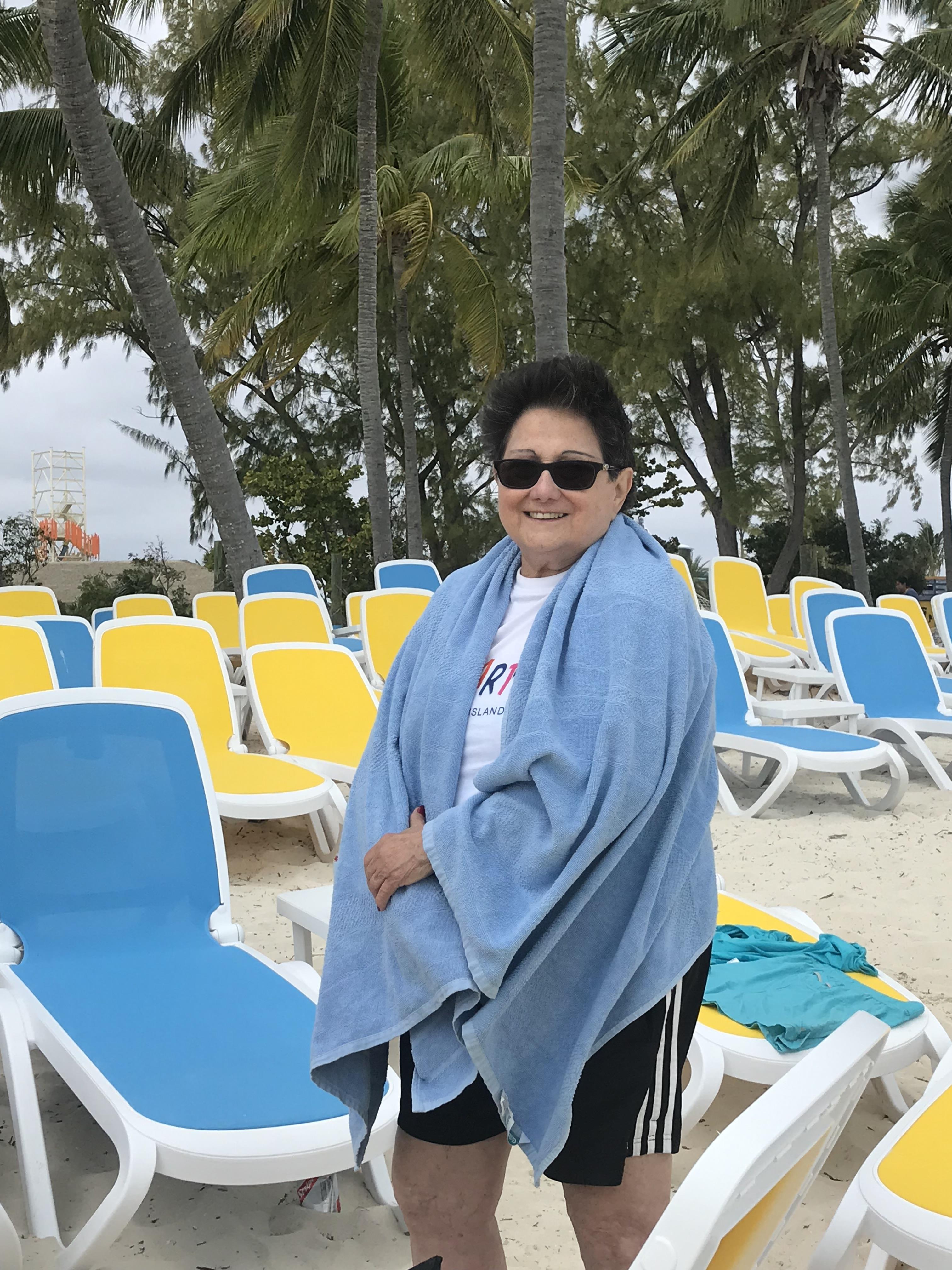 A woman relaxes on the beach in a towel, near colorful lounge chairs and palm trees.