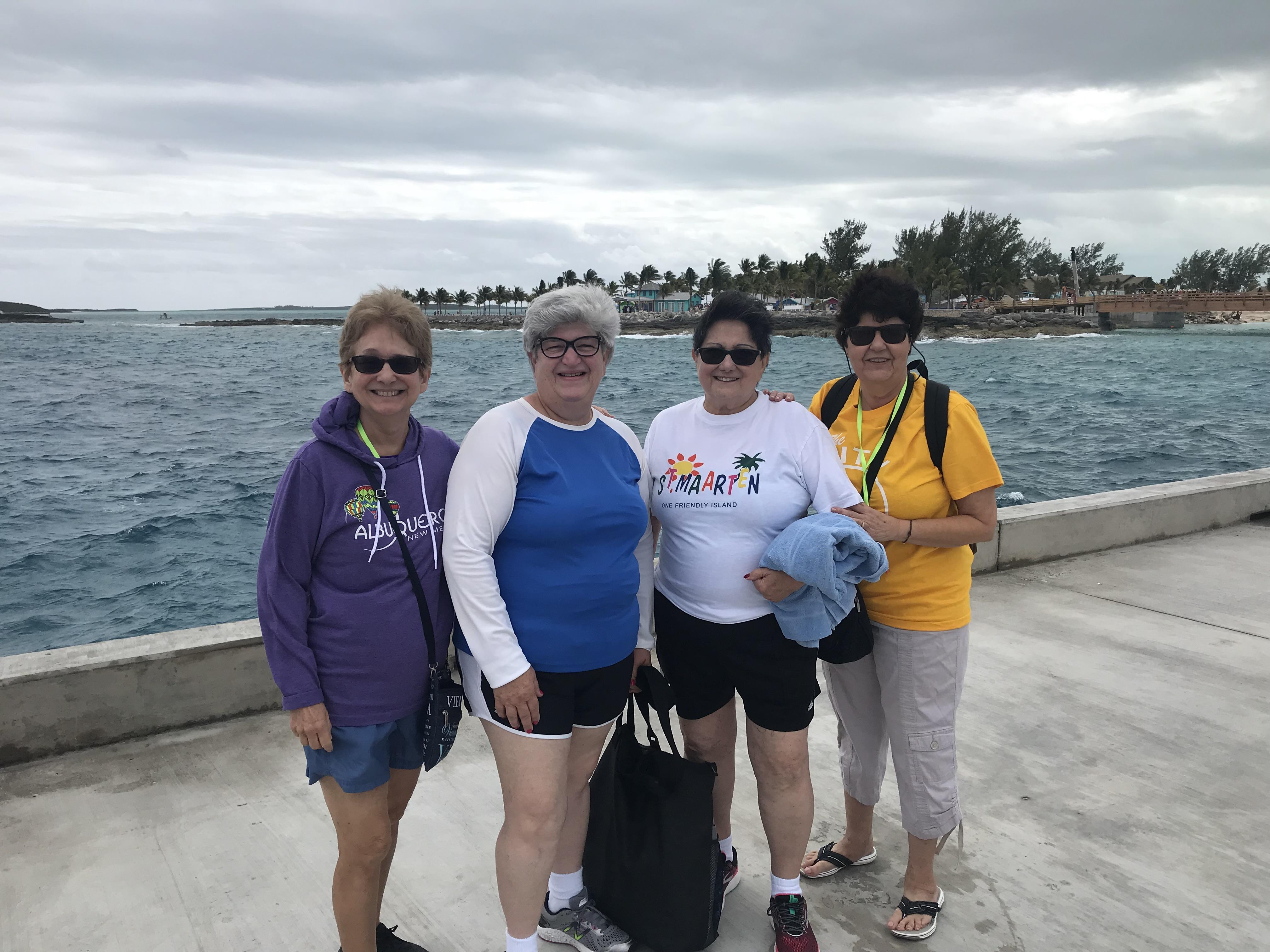 Four friends pose together by the ocean on a cloudy day, enjoying their vacation at a coastal spot.