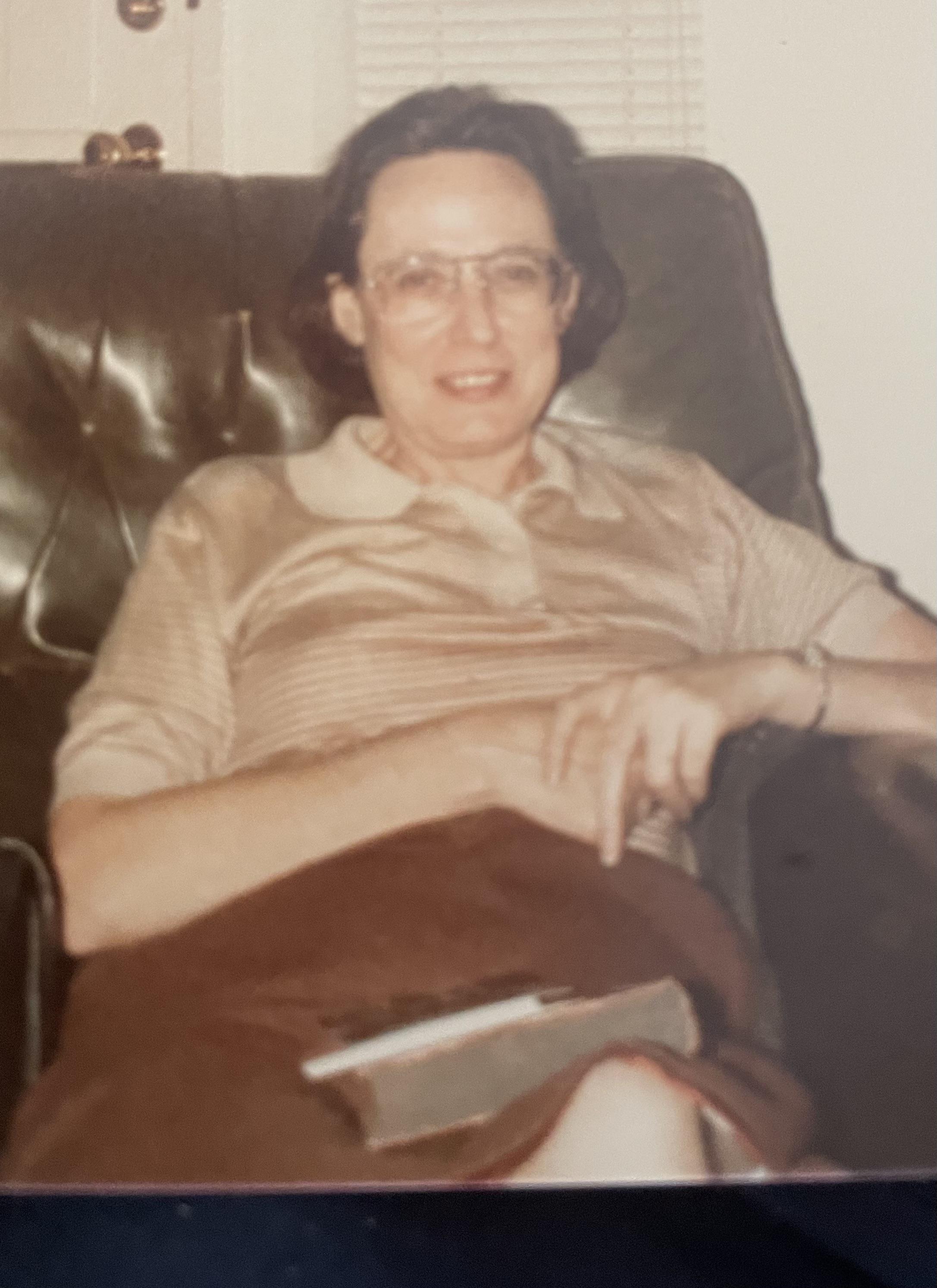 A senior woman sits comfortably on a sofa, engrossed in a book on a quiet afternoon.