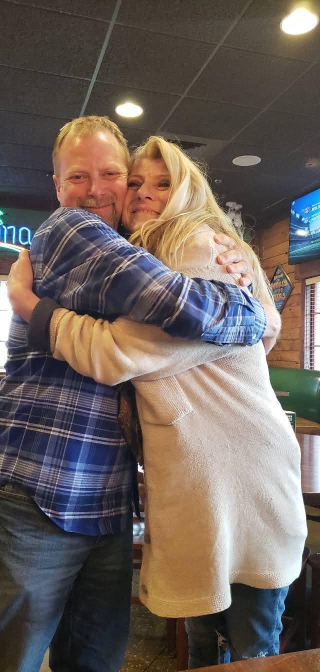 Two friends share a warm hug in a casual dining setting filled with laughter and joy.