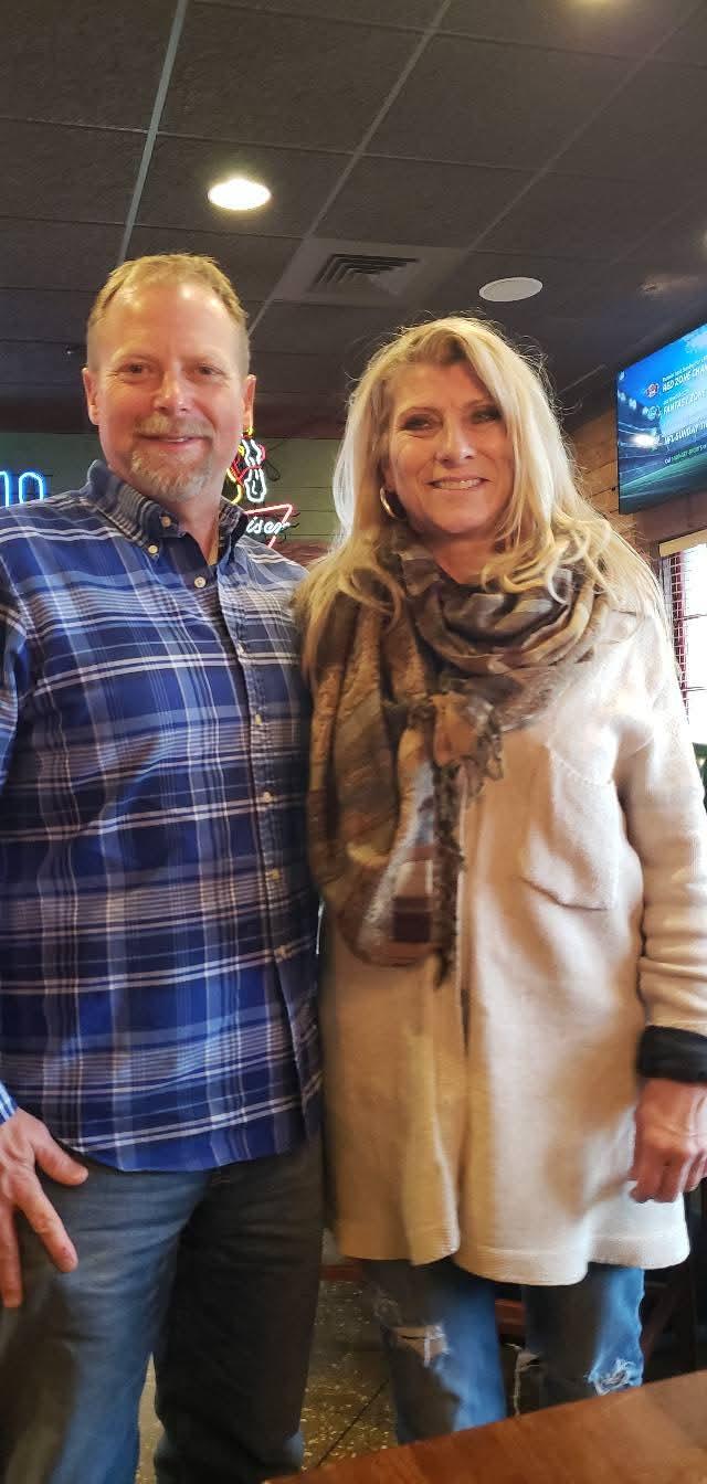 A smiling couple stands together in a vibrant restaurant, radiating happiness and warmth.