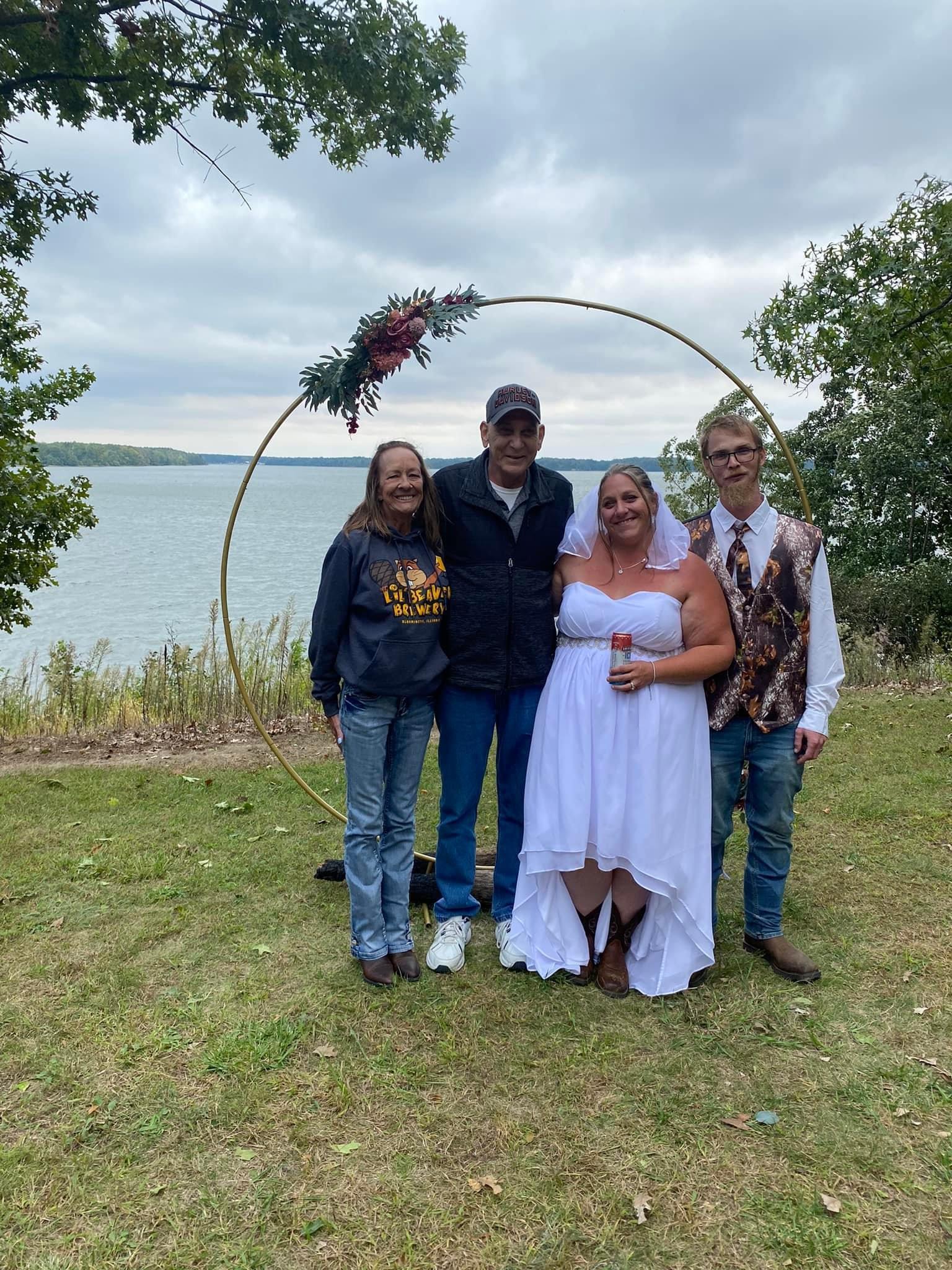 Group of four smiling friends gather by the lakeside for a joyful celebration among nature.