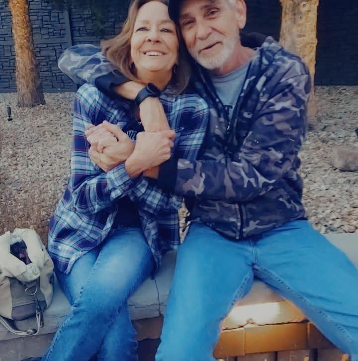 Two friends share a joyful embrace outdoors amidst natural surroundings and bright sunlight.