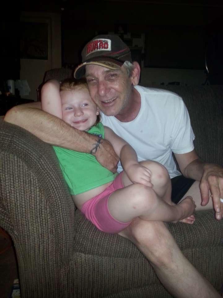 Grandfather and granddaughter enjoy a happy moment together, laughing on a couch in their home.