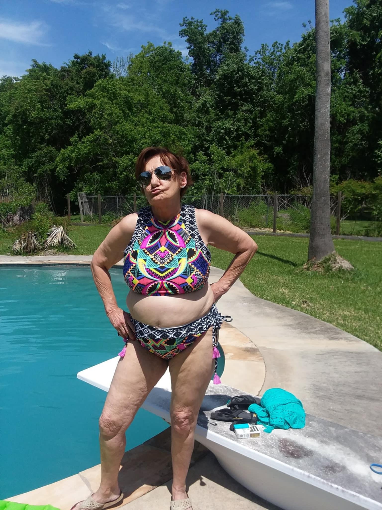 Woman relaxes by the poolside, showcasing her colorful swimsuit on a sunny day in the garden.