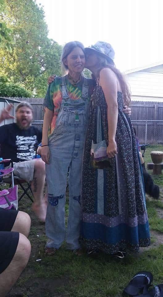 Two friends share a joyful moment while others relax in the background during a sunny afternoon.