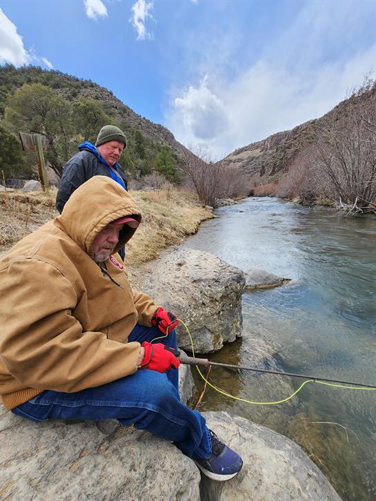 A man sitting on a rock with a fishing rod in the water