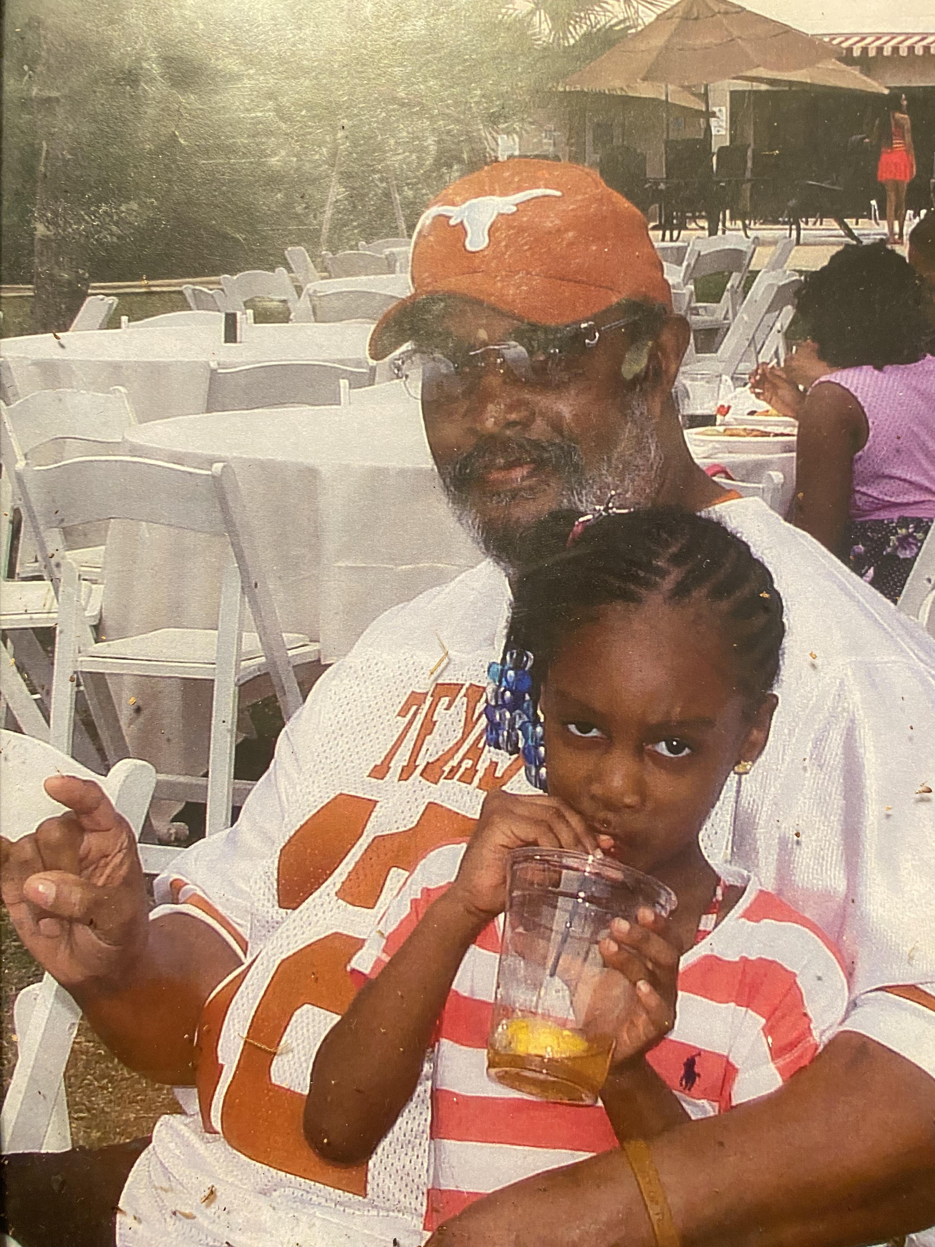 A grandfather and granddaughter sit together at an outdoor event.