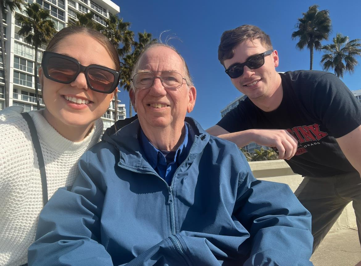 Joyful family poses together outdoors on a sunny day, showcasing smiles and a warm atmosphere.