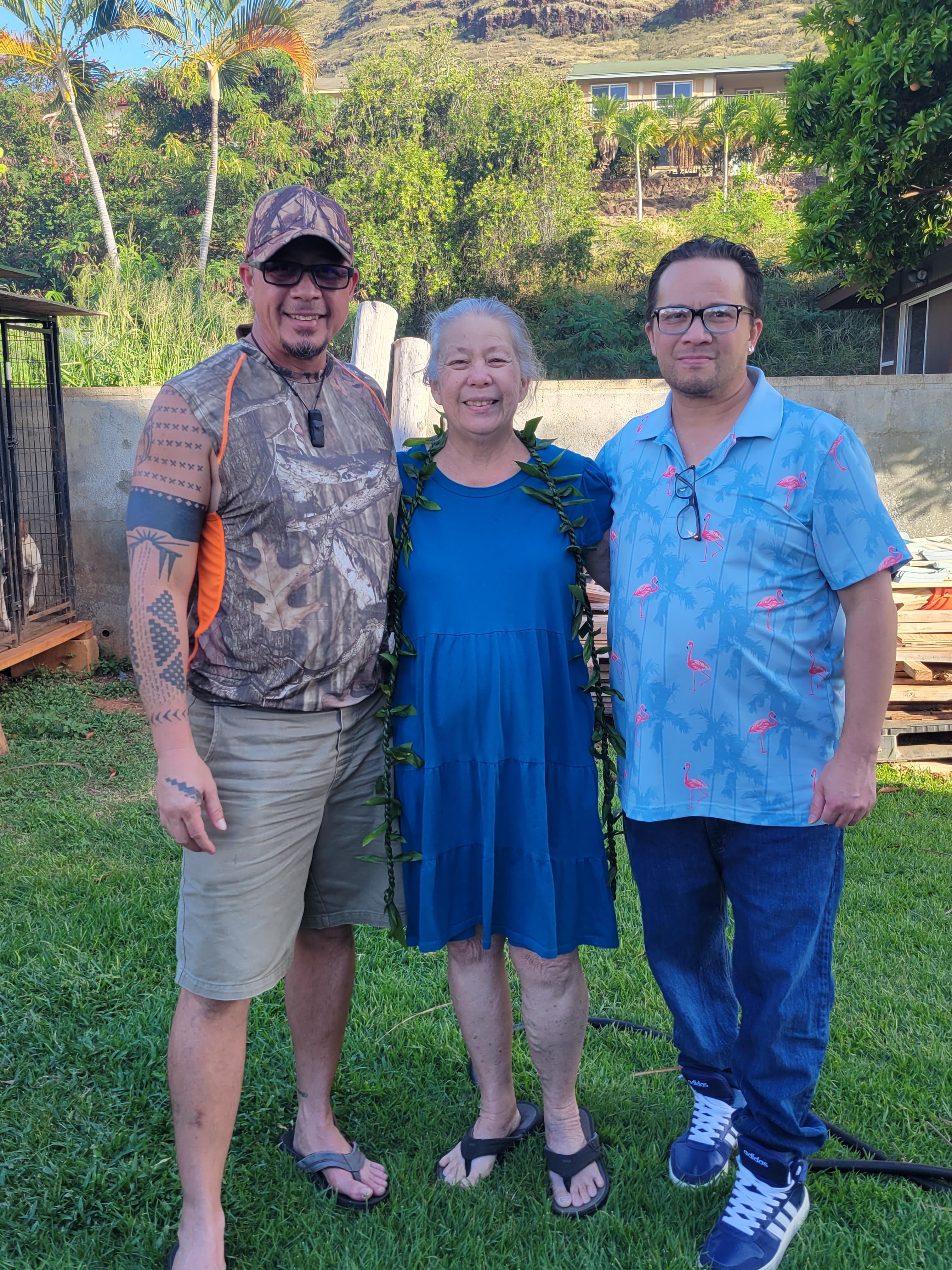 Three individuals stand together in a green outdoor area, enjoying a joyful moment.